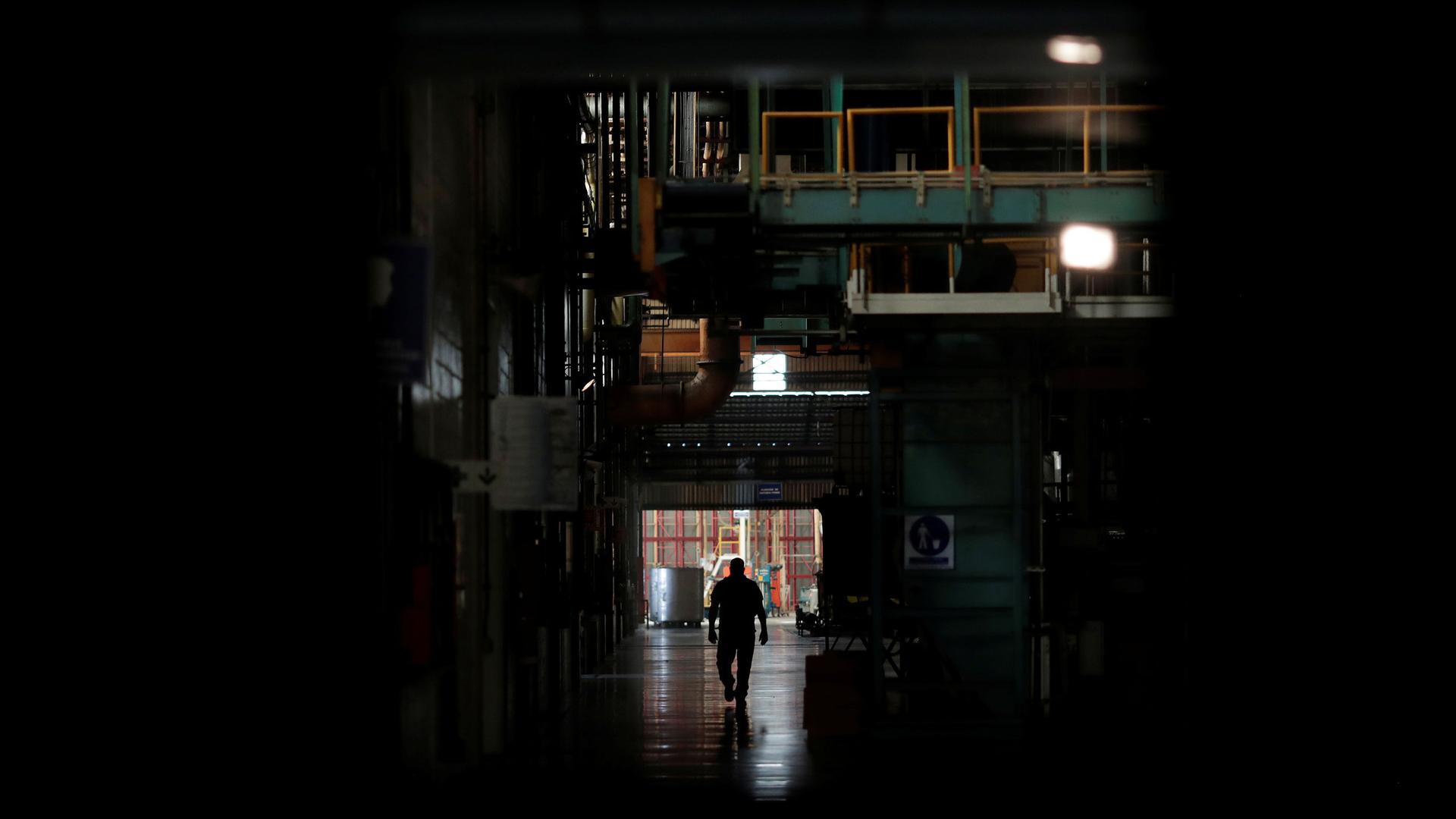 A man is shown in shadow walking past darked machinery.