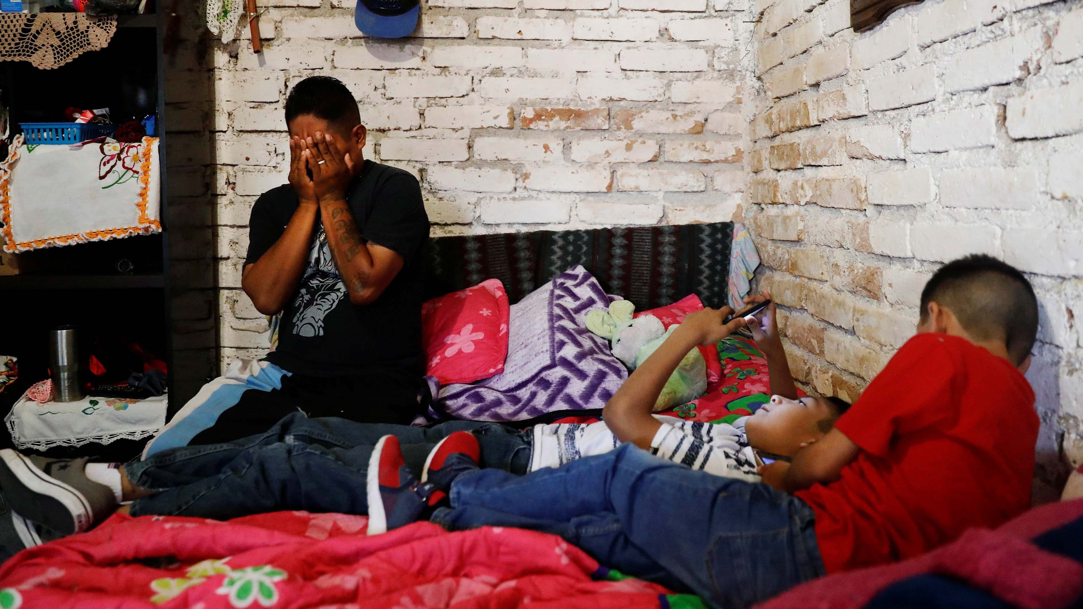 A man holds his face in his hands as two young boys lay on a bed