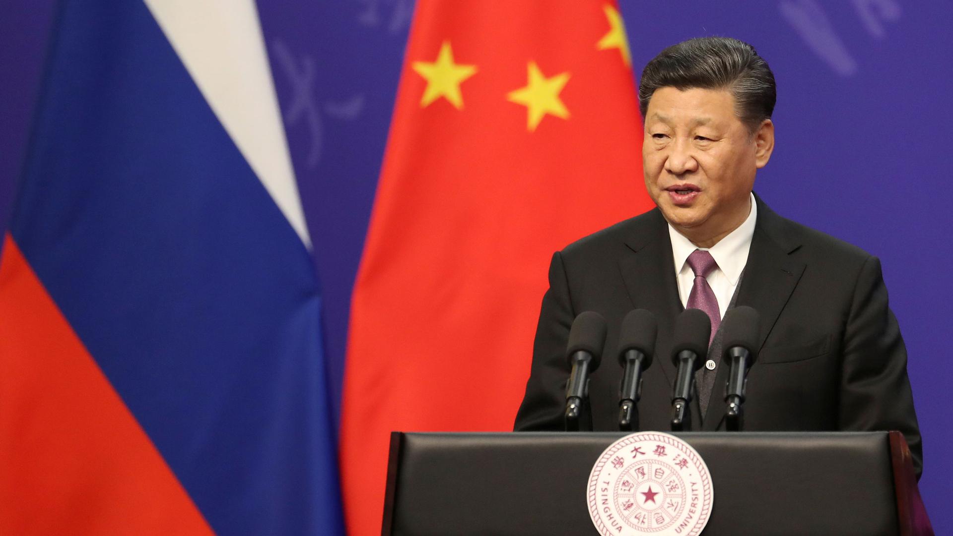 Chinese President Xi Jinping is shown standing at a podium with four microphones.