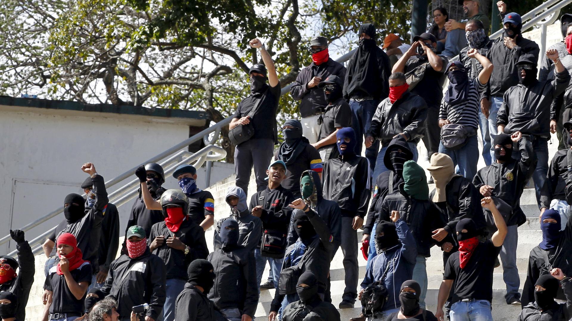 Young men wearing black stand on steps and raise fists in air. 