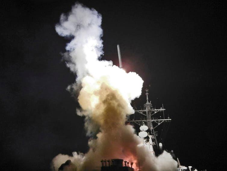 Smoke fills the air as a missile is launched from a military boat at night.