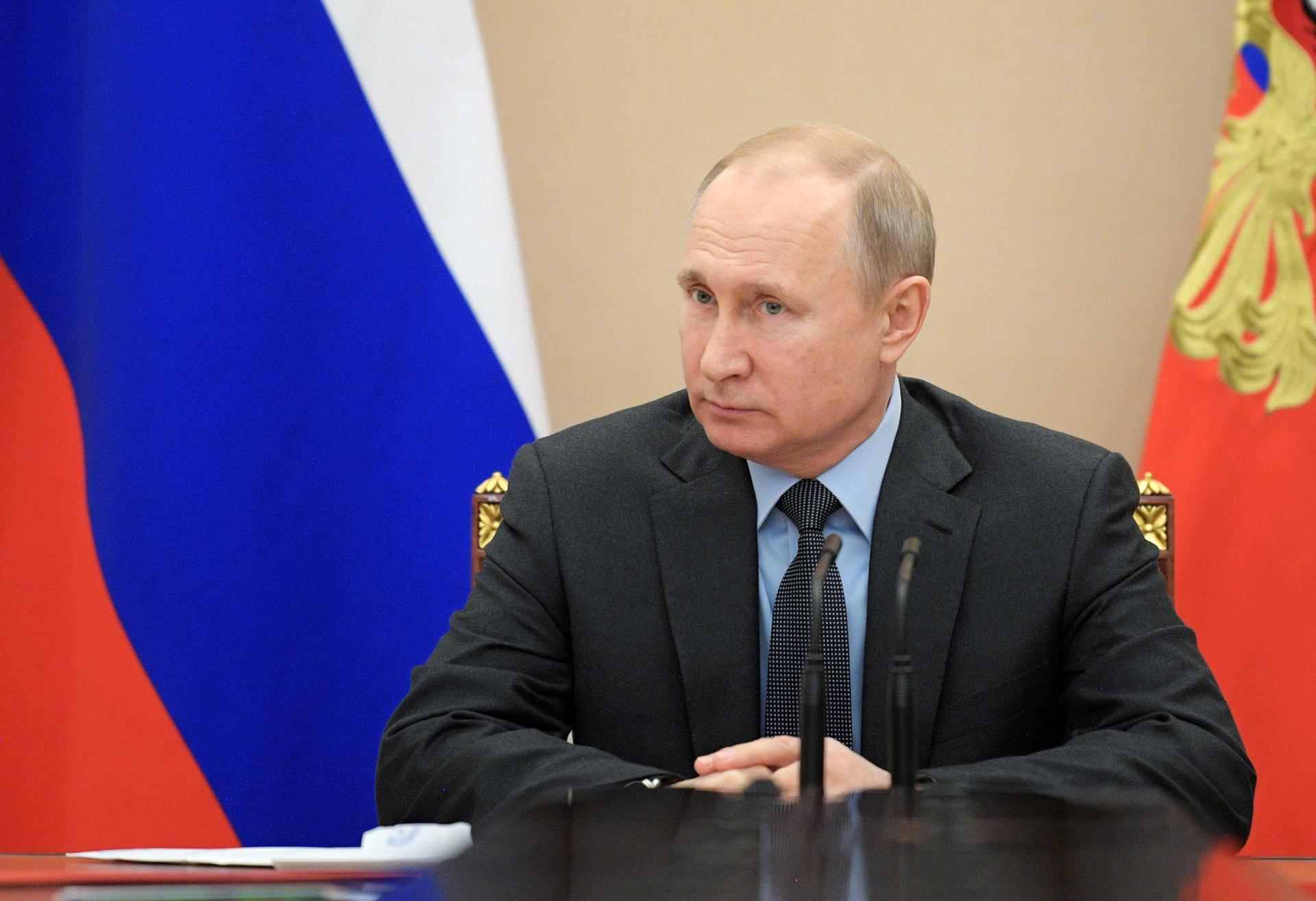 Vladimir Putin sits at a desk with the Russian flag behind him. 