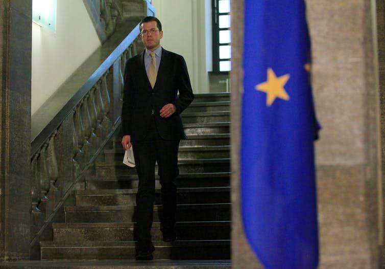 A man stands on a staircase next to a European Union flag.