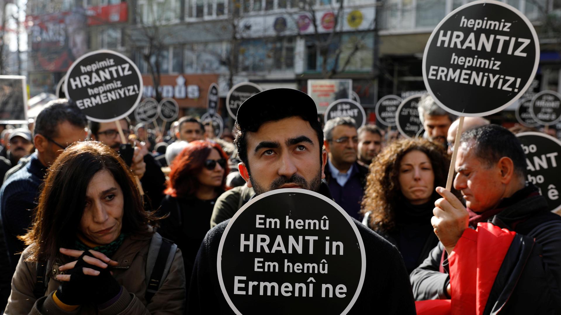Protesters carry black sign with white writing in support of slain Armenian journalist. 