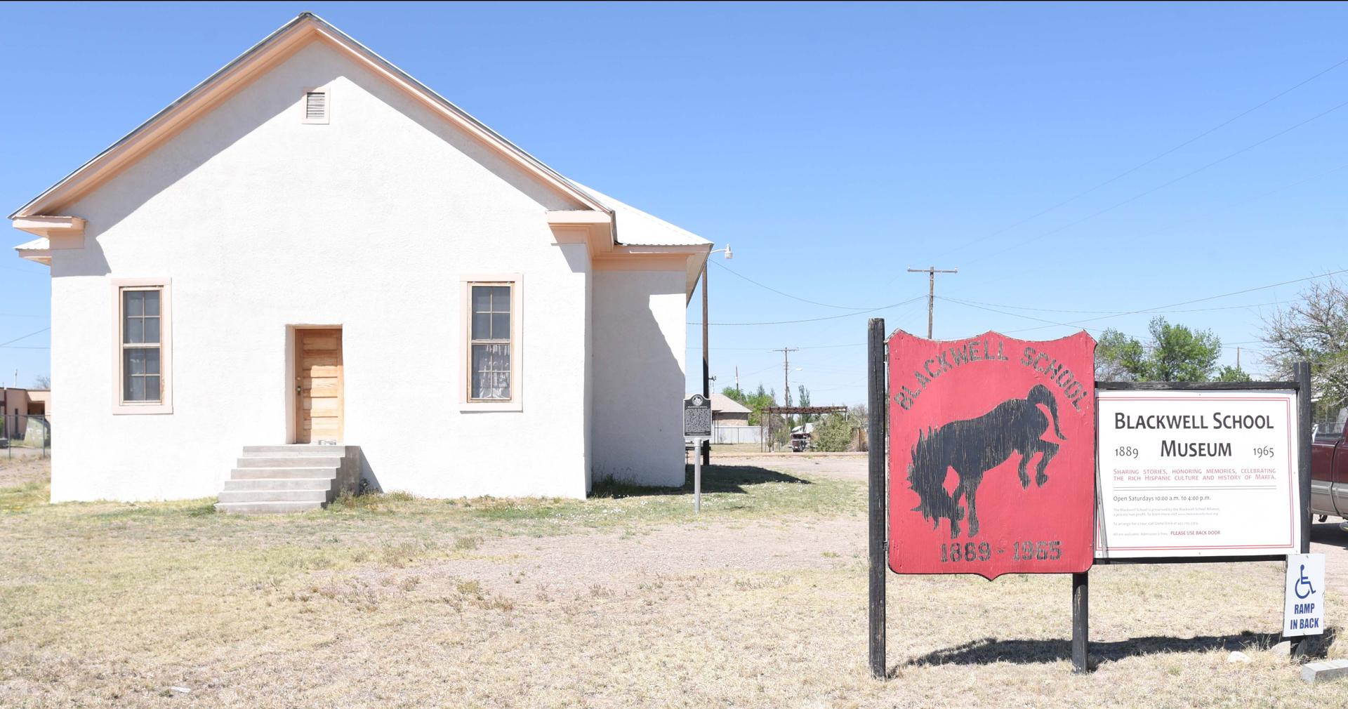 An adobe school house with a sign in front