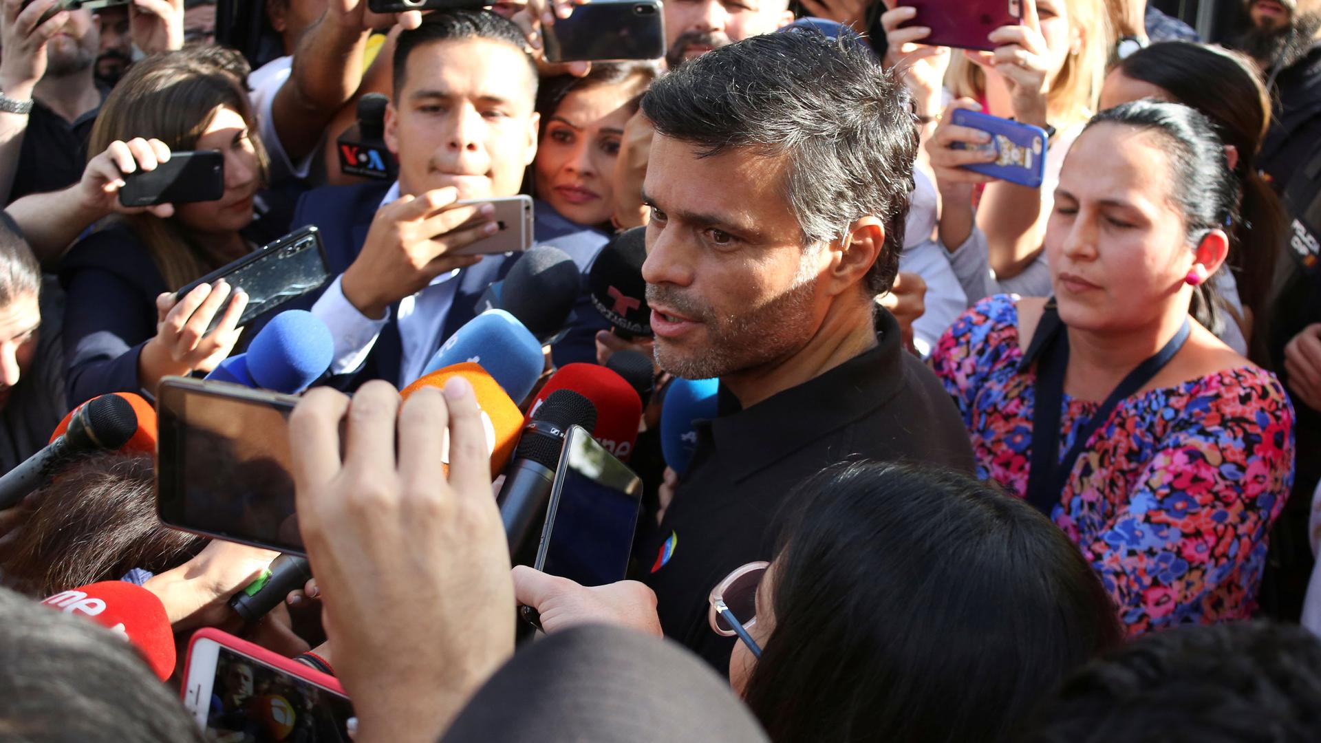 Venezuelan opposition politician Leopoldo López is shown in a crowd of people speaking into several microphones.