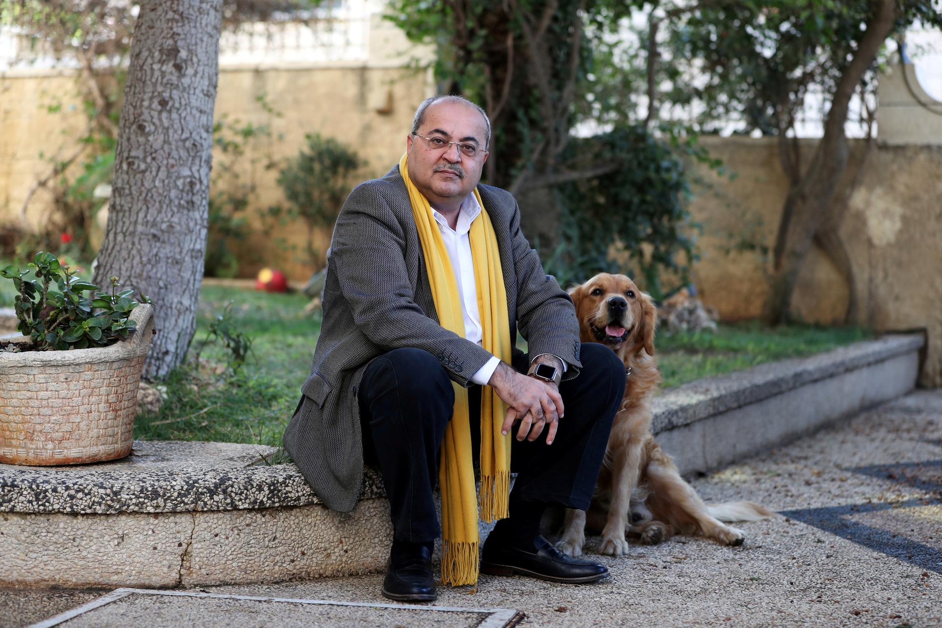Arab politician wears yellow scarf in a suit with his dog and sits on a curb.