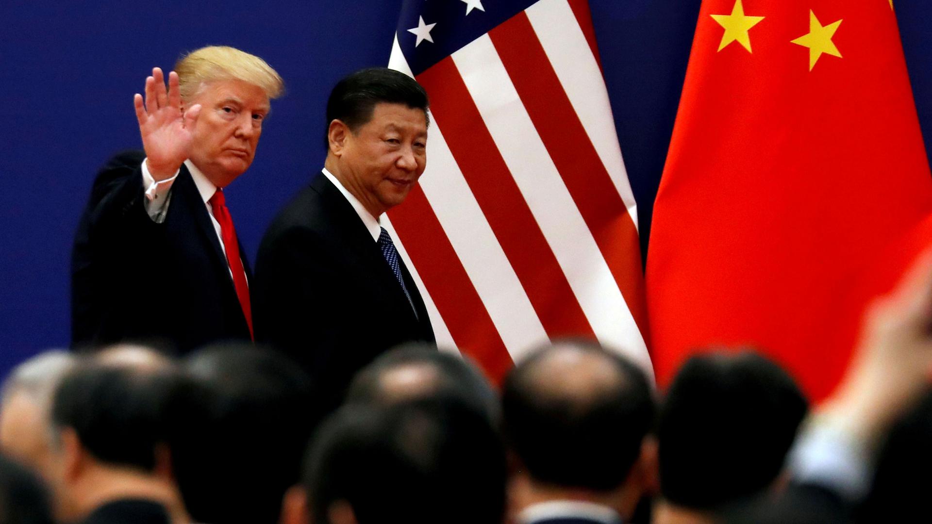 US President Donald Trump and China's President Xi Jinping are shown walking with the US and China flags in the background and Trump waving.
