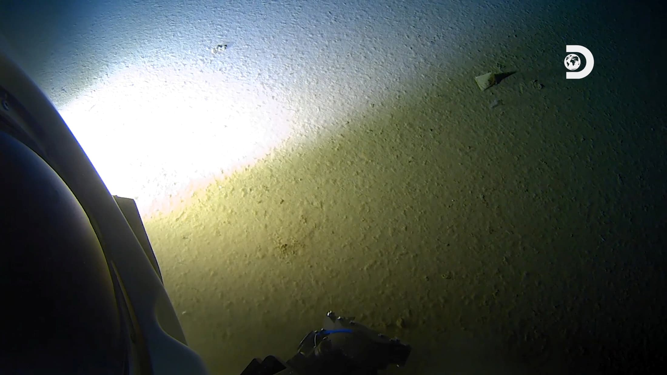 A submarine shines a light on small pieces of garbage in the dark depths of the ocean.