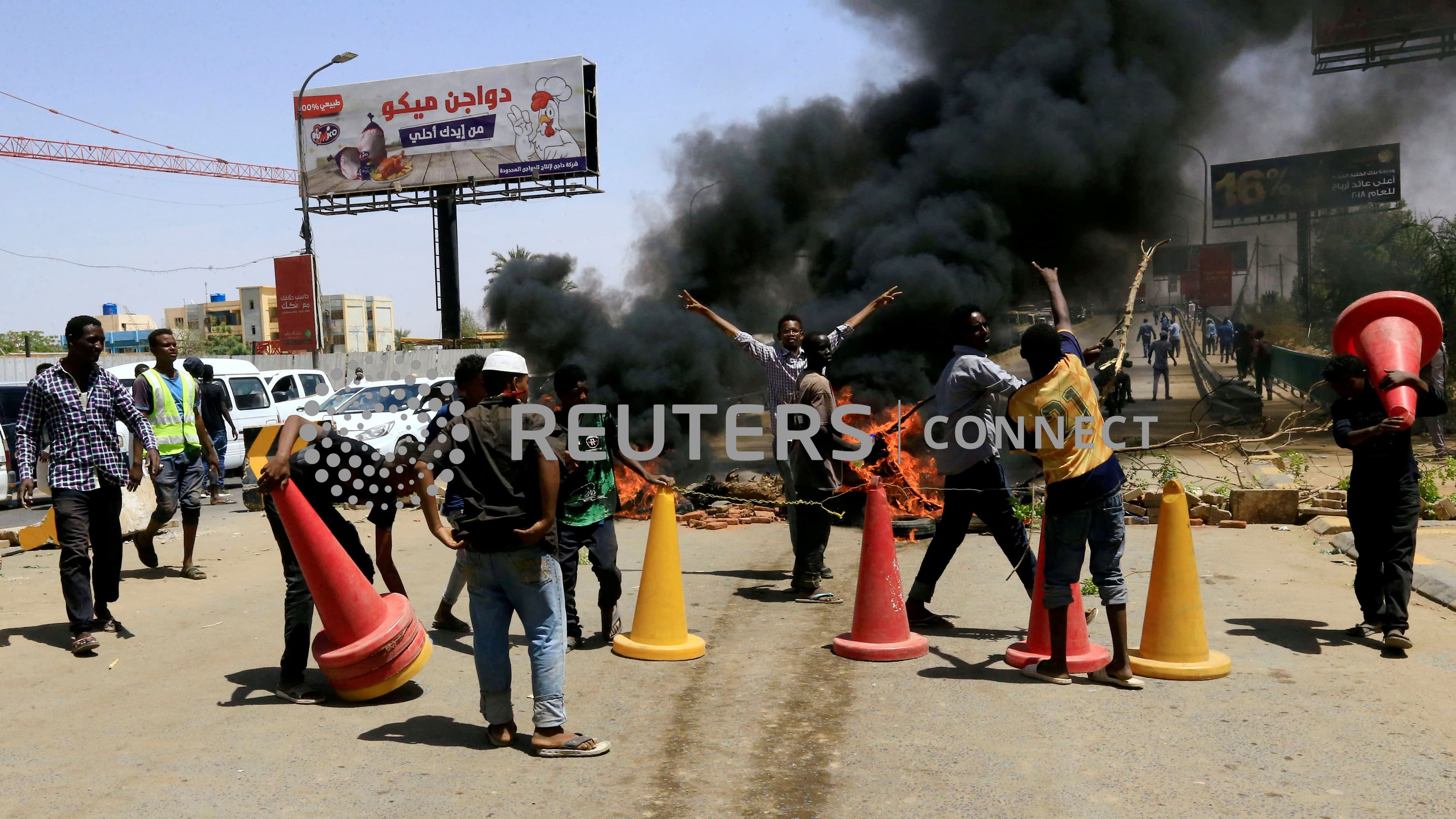 Men and traffic cones are around a tire fire with a plume of black smoke