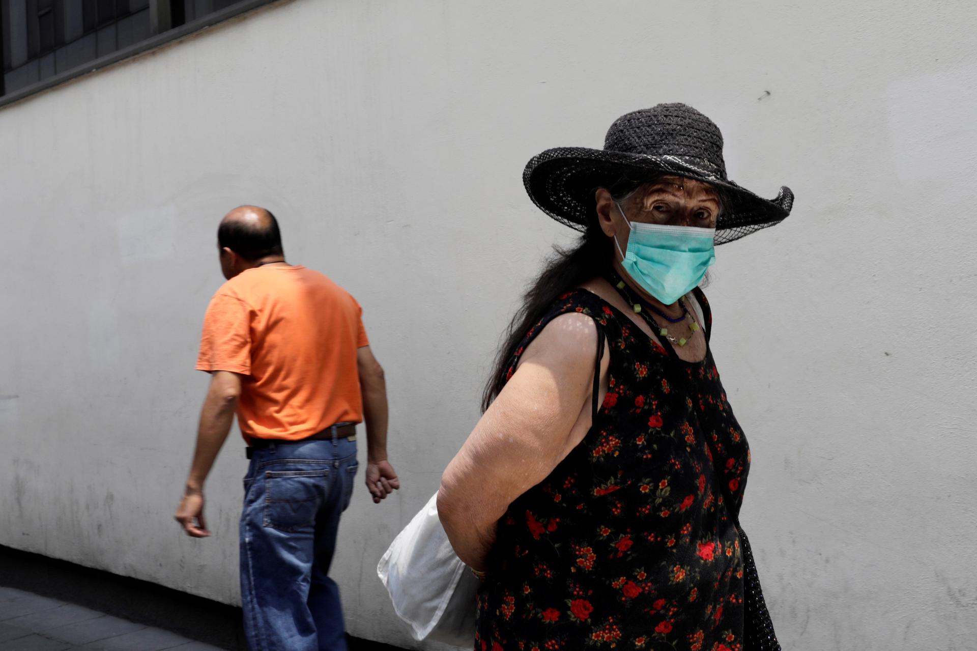 An older woman wears a surgical mask as she looks at the camera