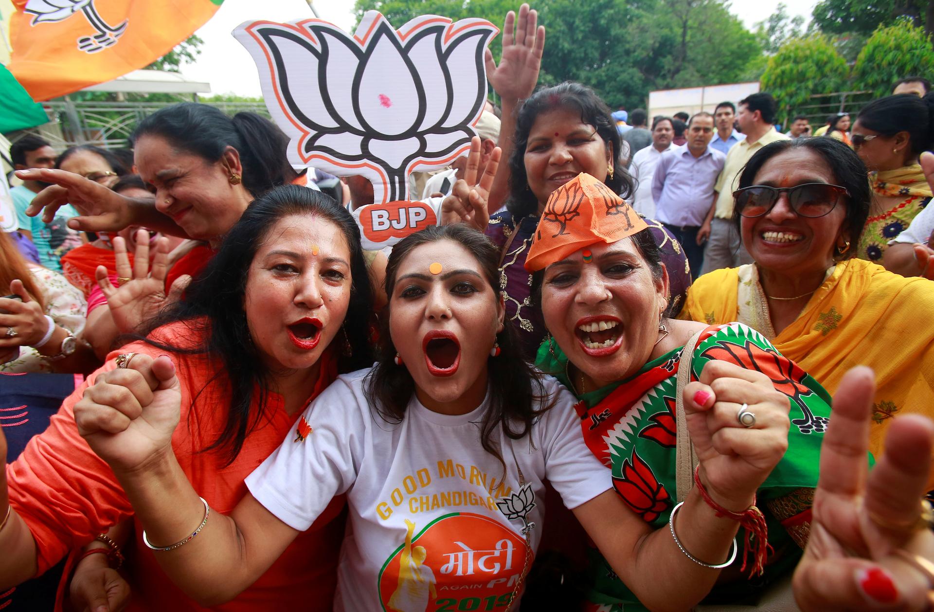 Three women cheer during election results in India wearing orange for BJP.