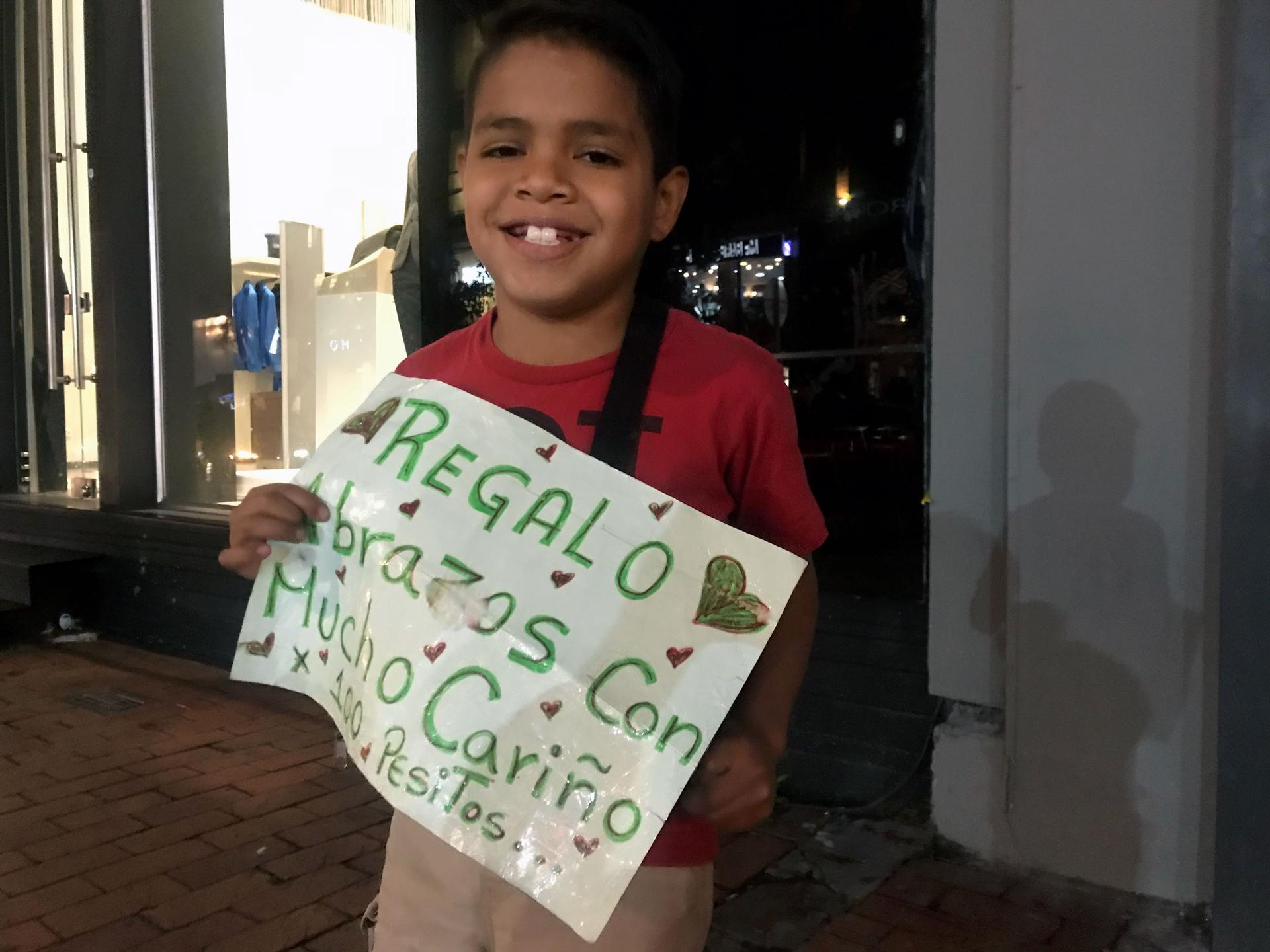 A young boy holds a sign selling hugs for 100 pesos