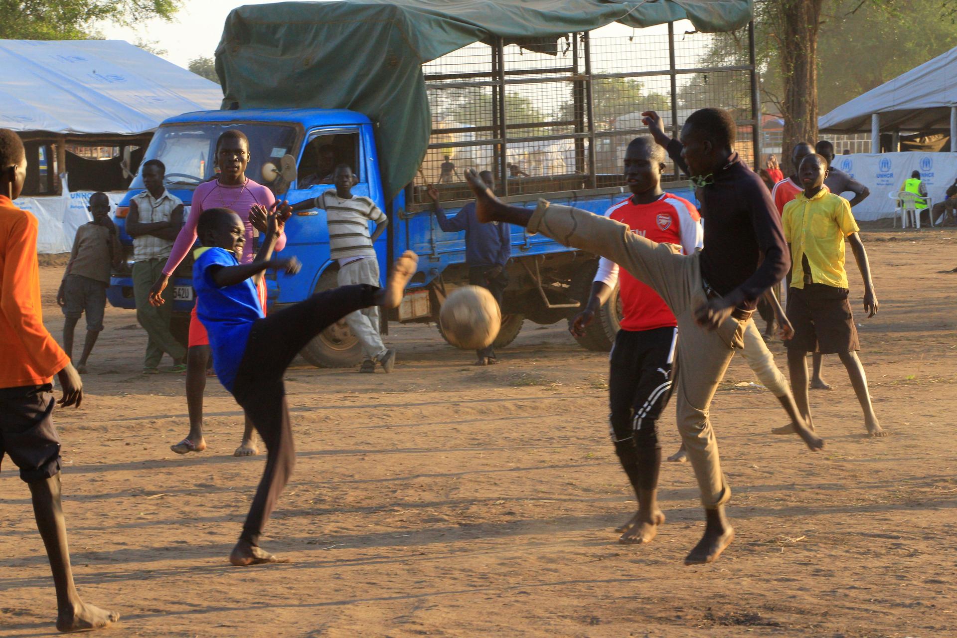 youth play soccer near trucks at refugee camp