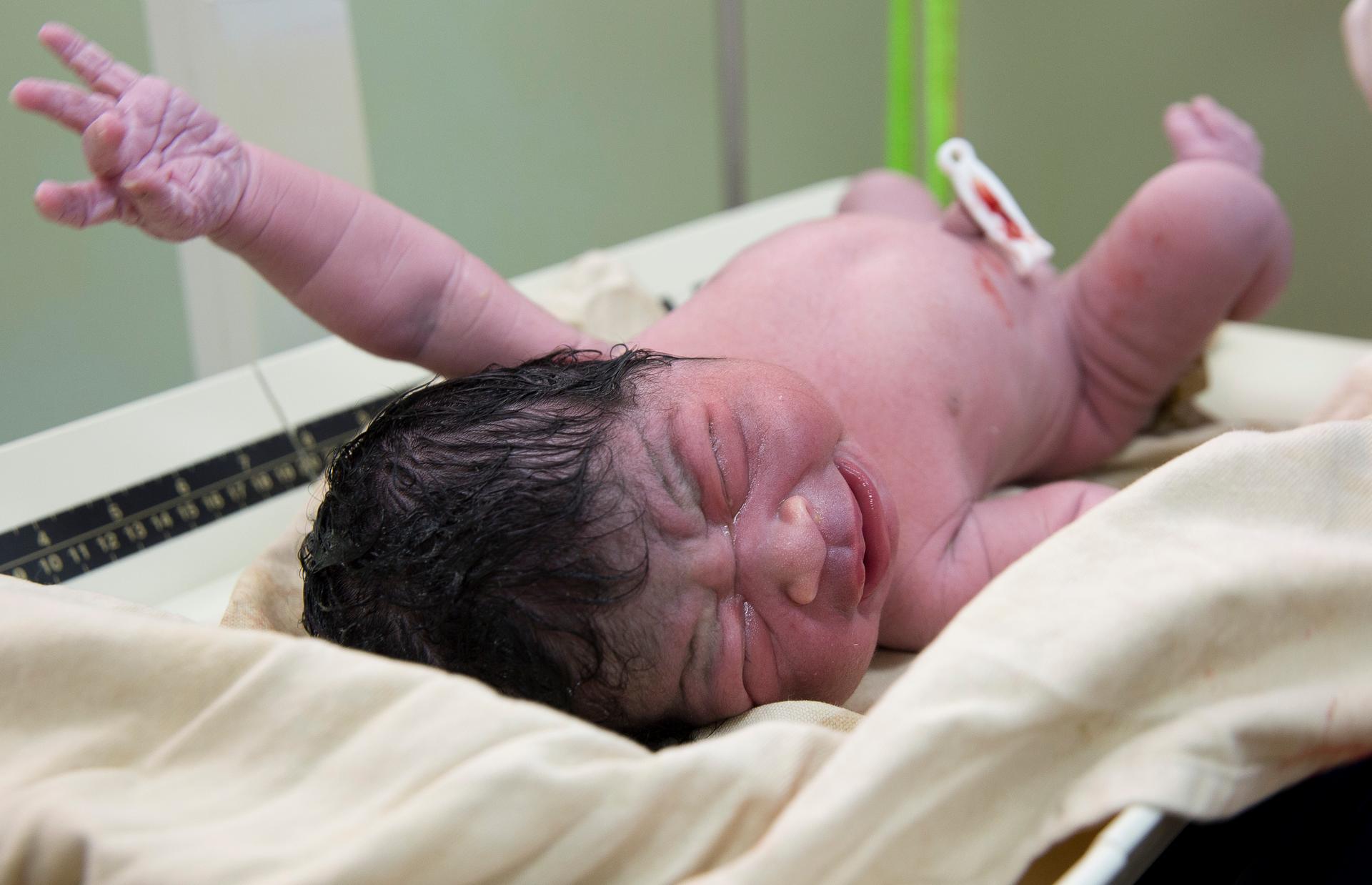 newborn baby with black wet hair and fist raised and clipped belly button