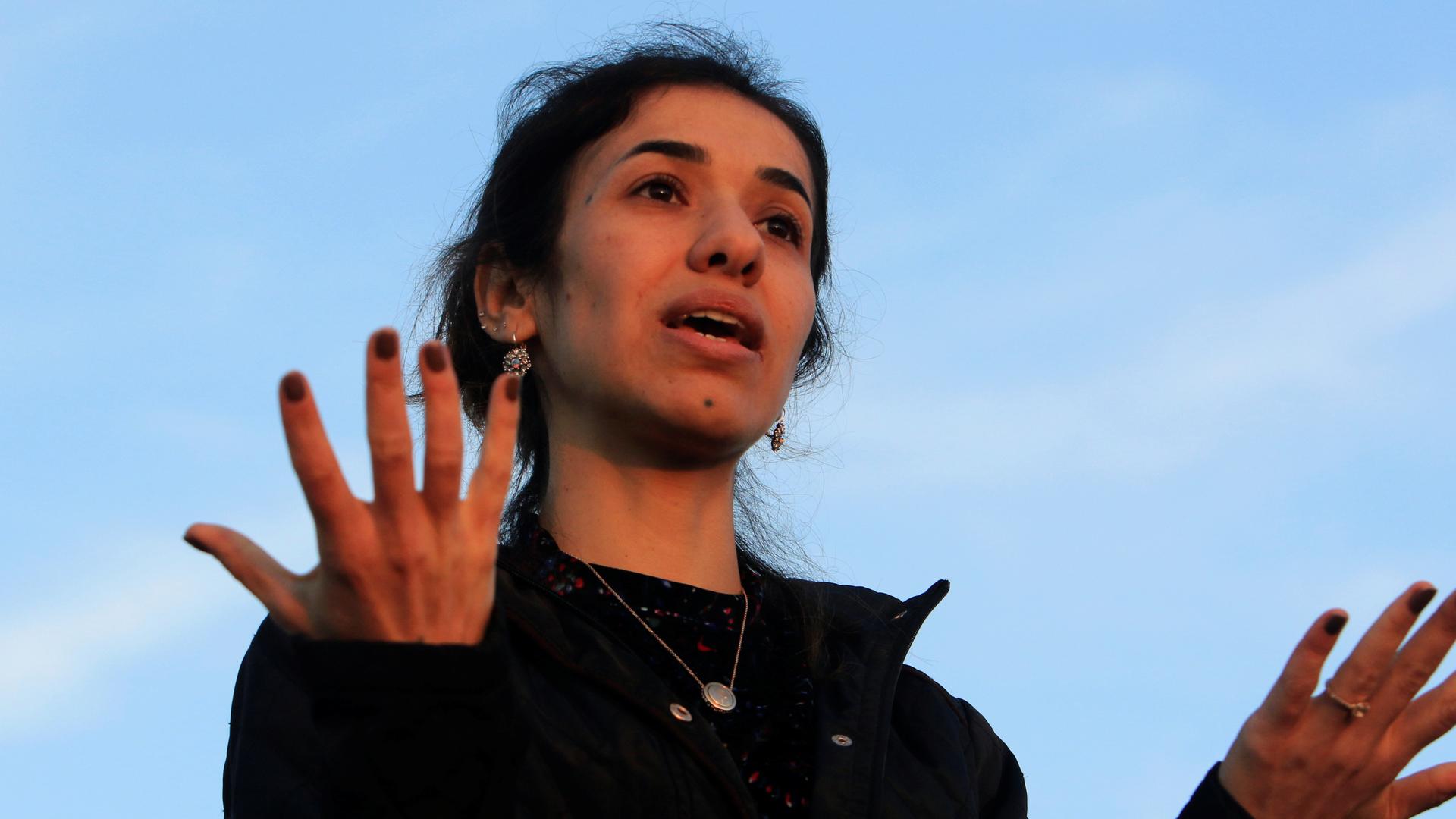 Nadia Murad gestures with her hands against a blue sky. 
