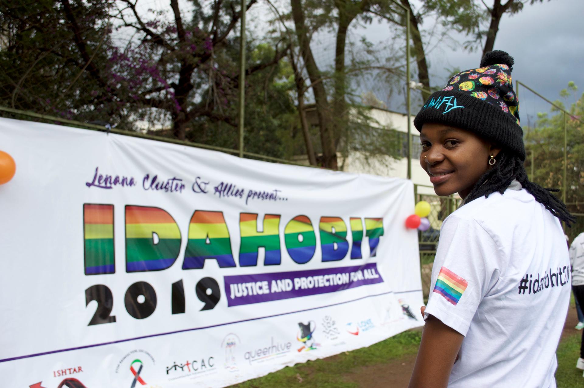 A queer person in Kenya stands near rainbow banner.