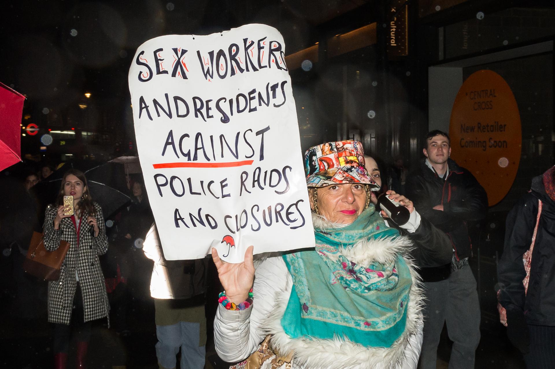 A woman holds a sign that says "Sex workers and residents against police raids and closures."