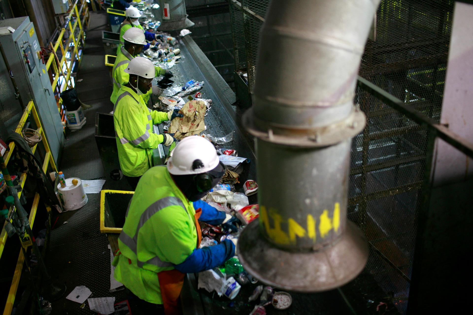 Workers in a dark building sort trash from a conveyor belt. 