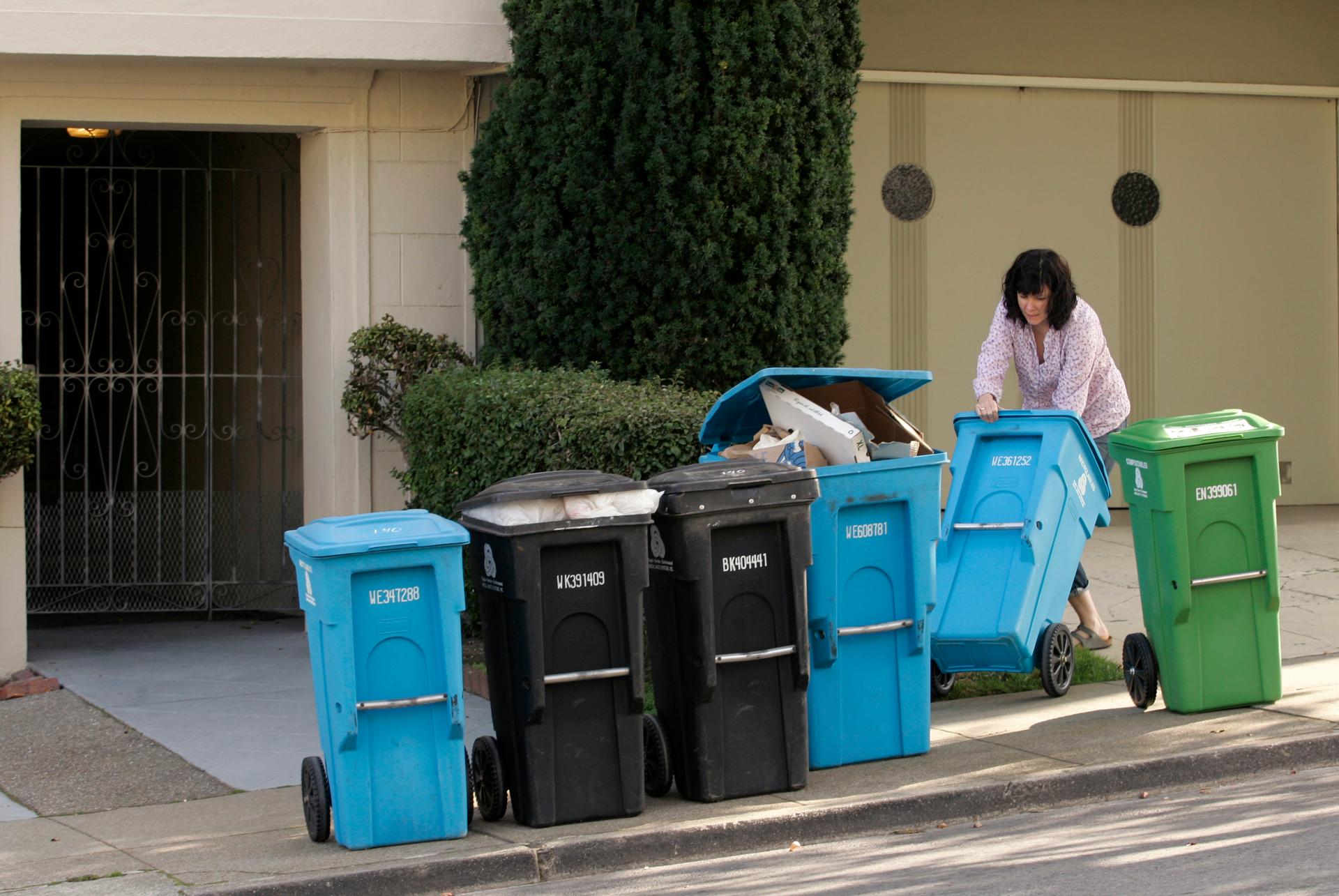 A woman puts different large garbage and recycling containers on a sidewalk.