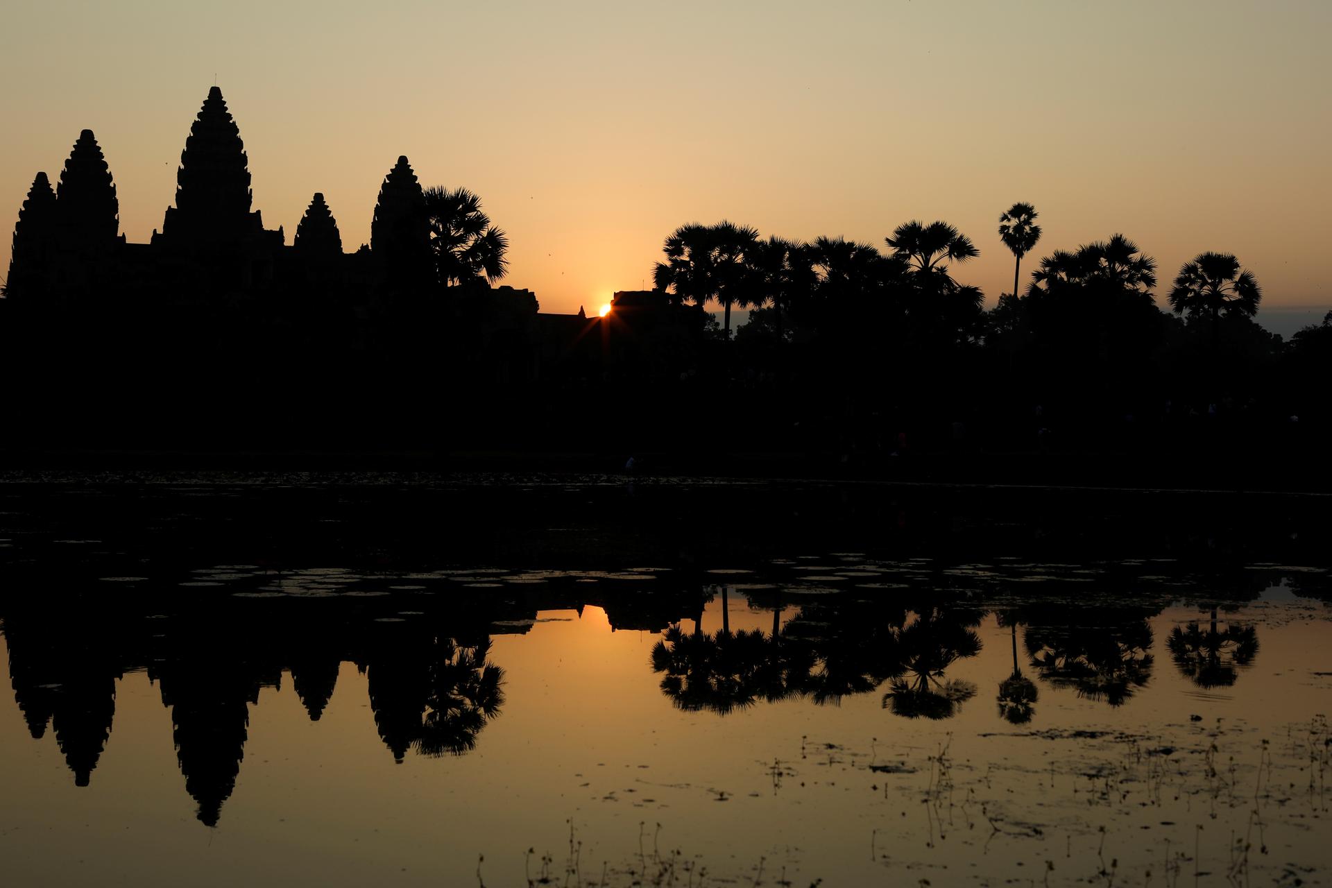 Angkor Wat is shown by a pond at sunrise.
