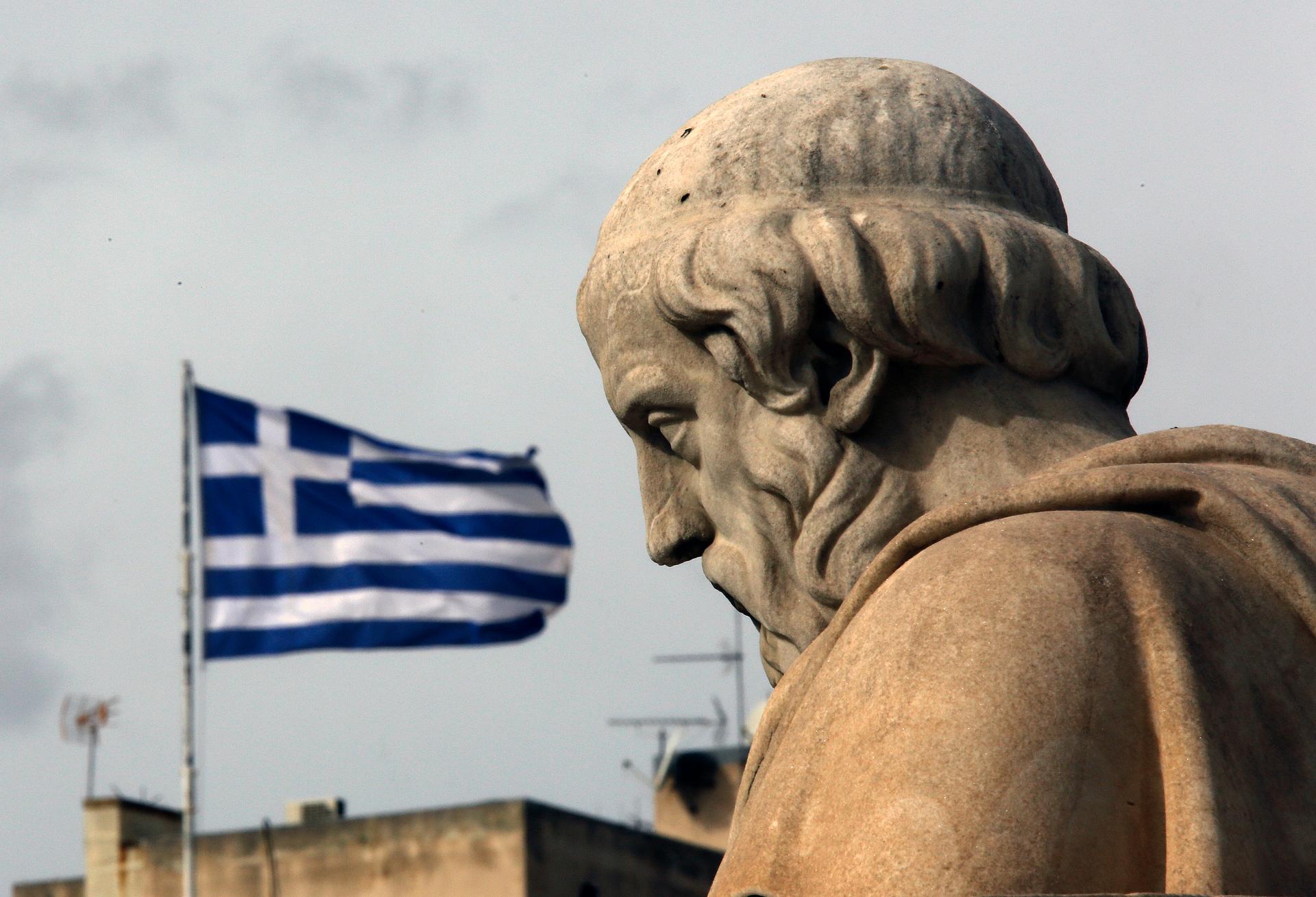 A marble statue stands in front of a Greek flag. 