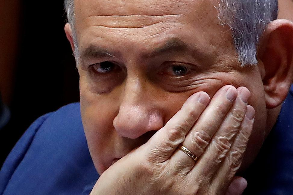 Benjamin Netanyahu sits with his hand covering his mouth.