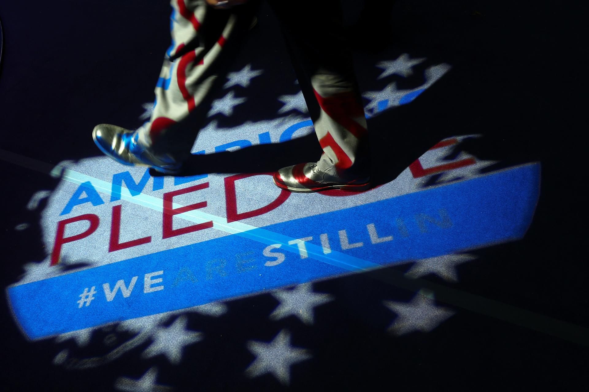 A man walks over a projection on the floor reading "America's pledge #wearestillin"