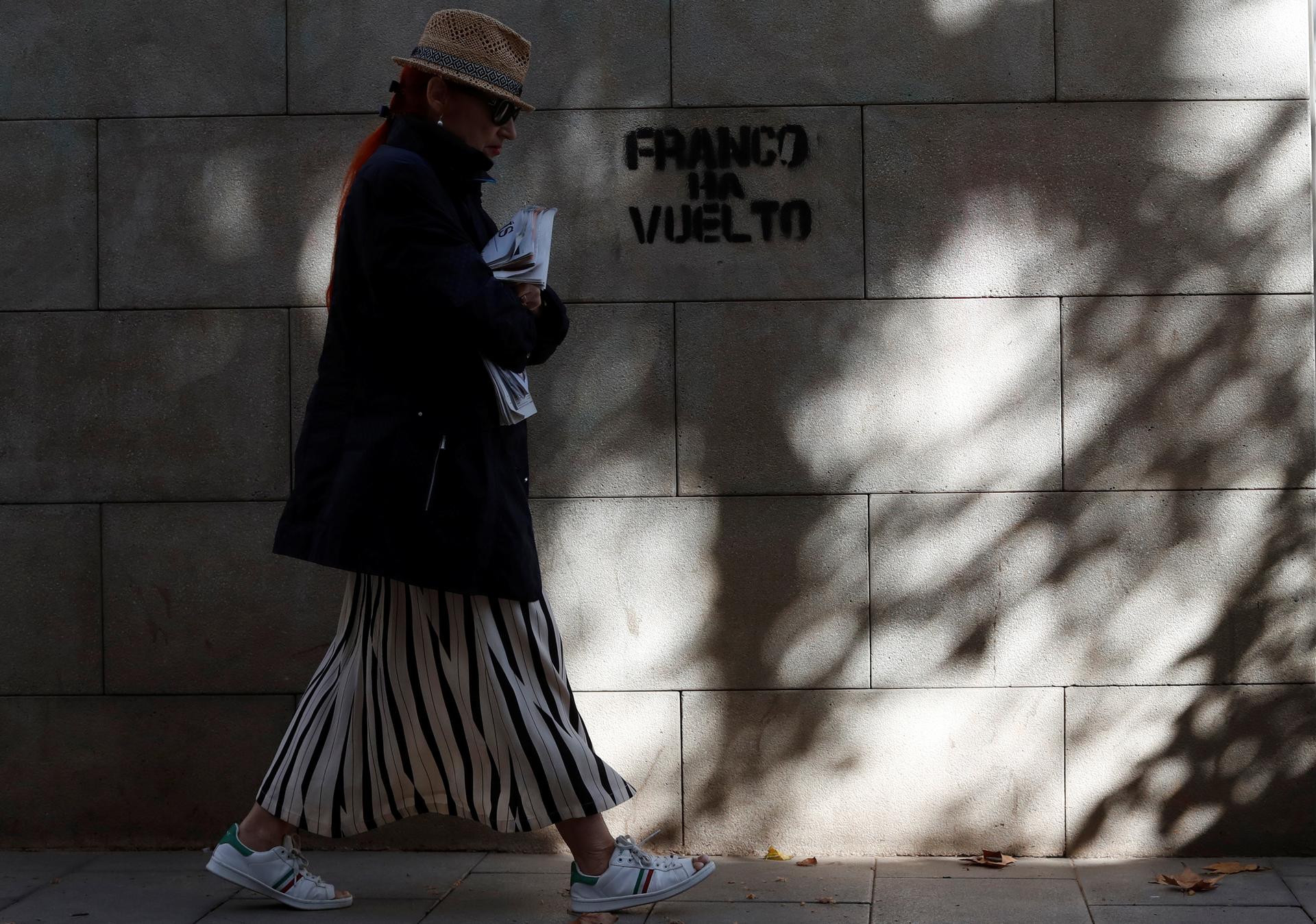 A woman walks past a graffiti which reads 