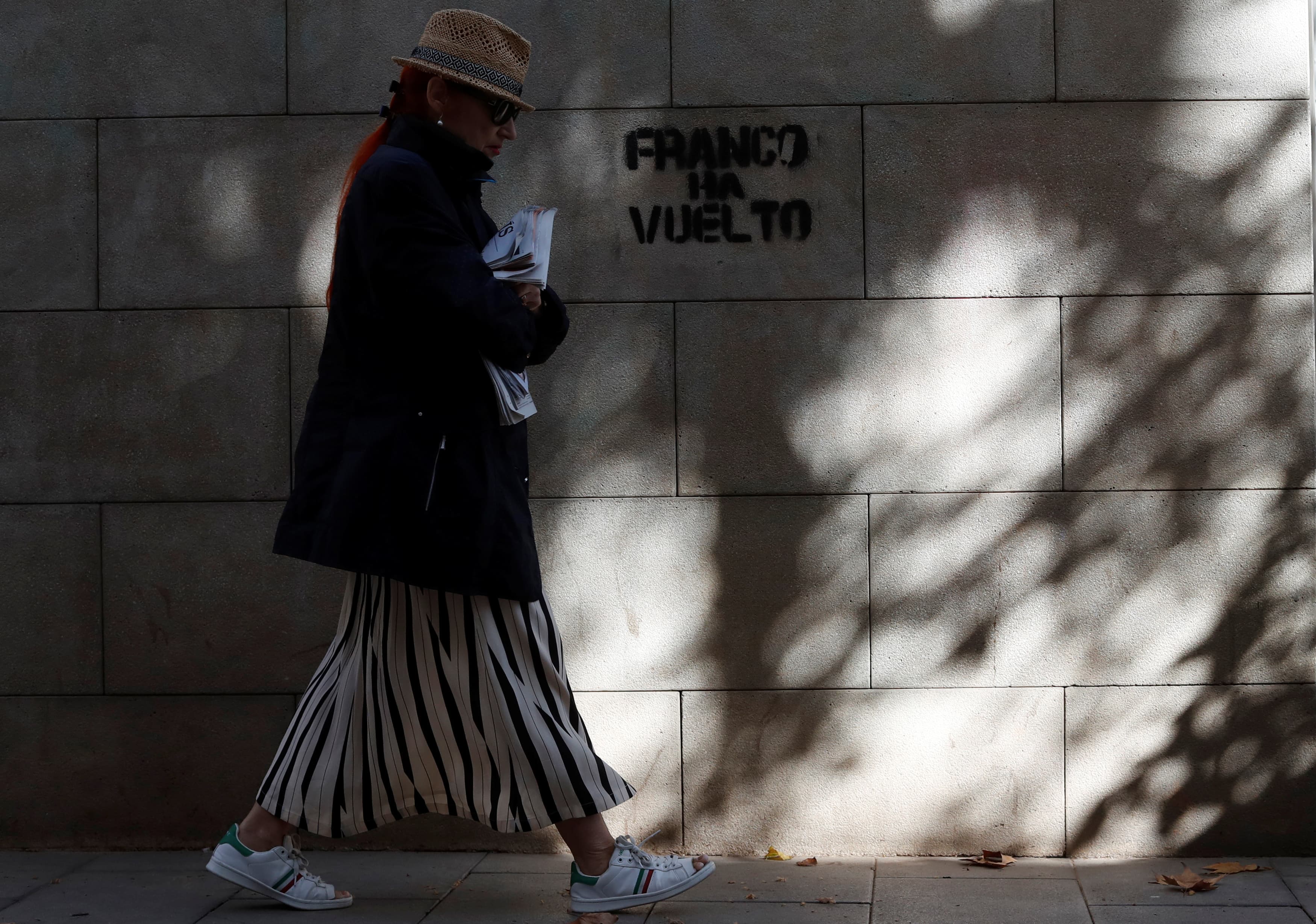 A woman walks past a graffiti which reads