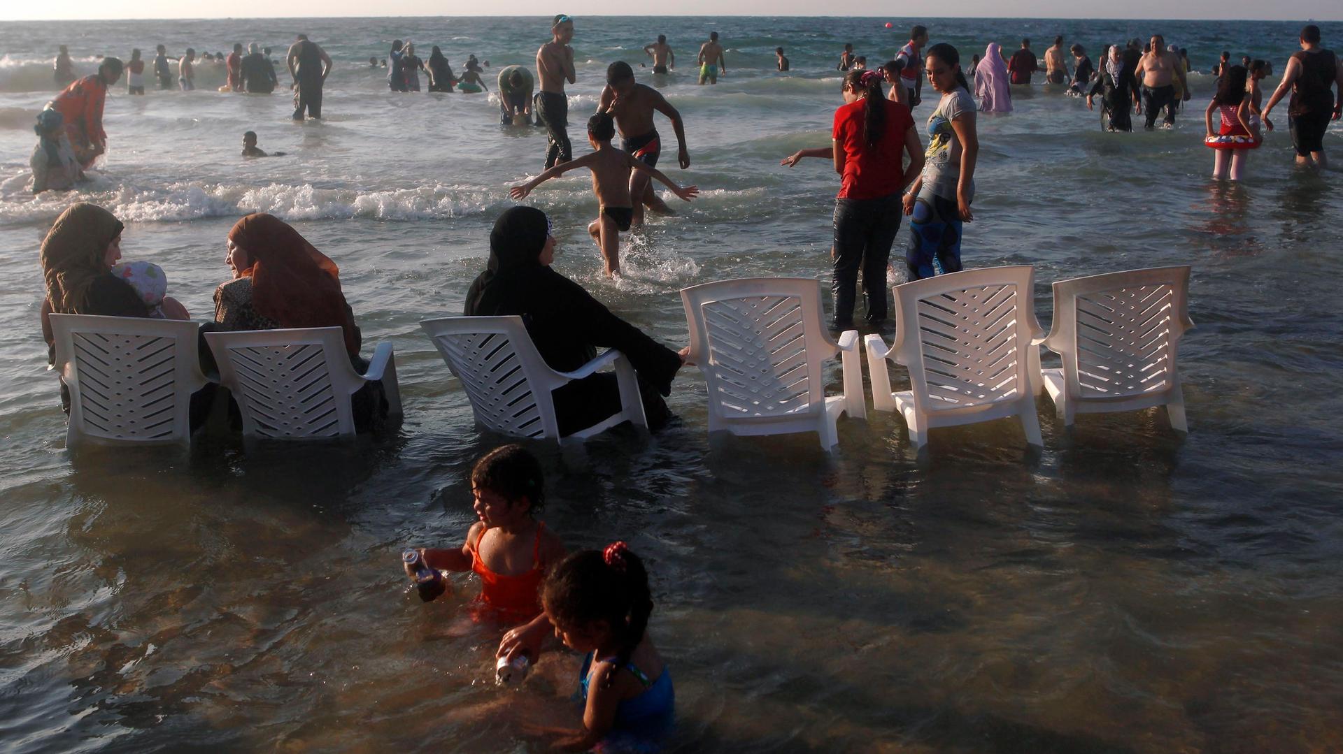 Women wearing headscarves sit in chairs at a public beach in Alexandria, Egypt