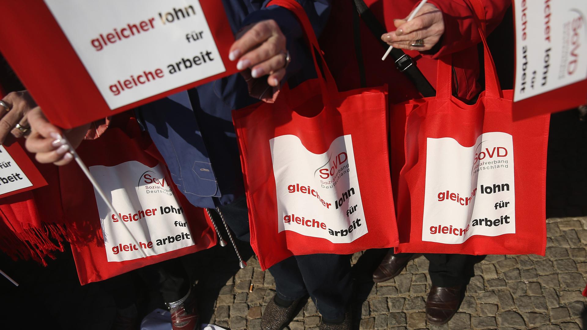 Women hold bags and signs that read: "Same pay for same work" at a rally for equal pay in Berlin, Germany, 2015.