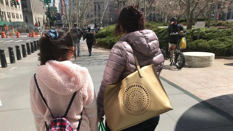 A girl and a woman carry bags and have their back turned to the camera on a city street