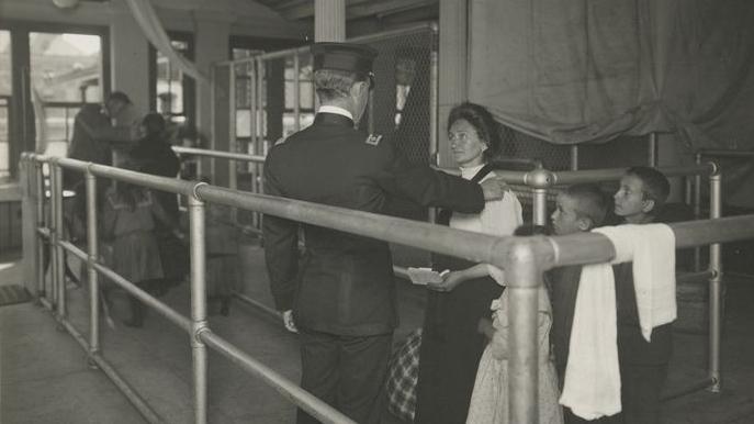 A black and white historical photo of a uniformed man with his hand on a woman's shoulder while young boys look on. 