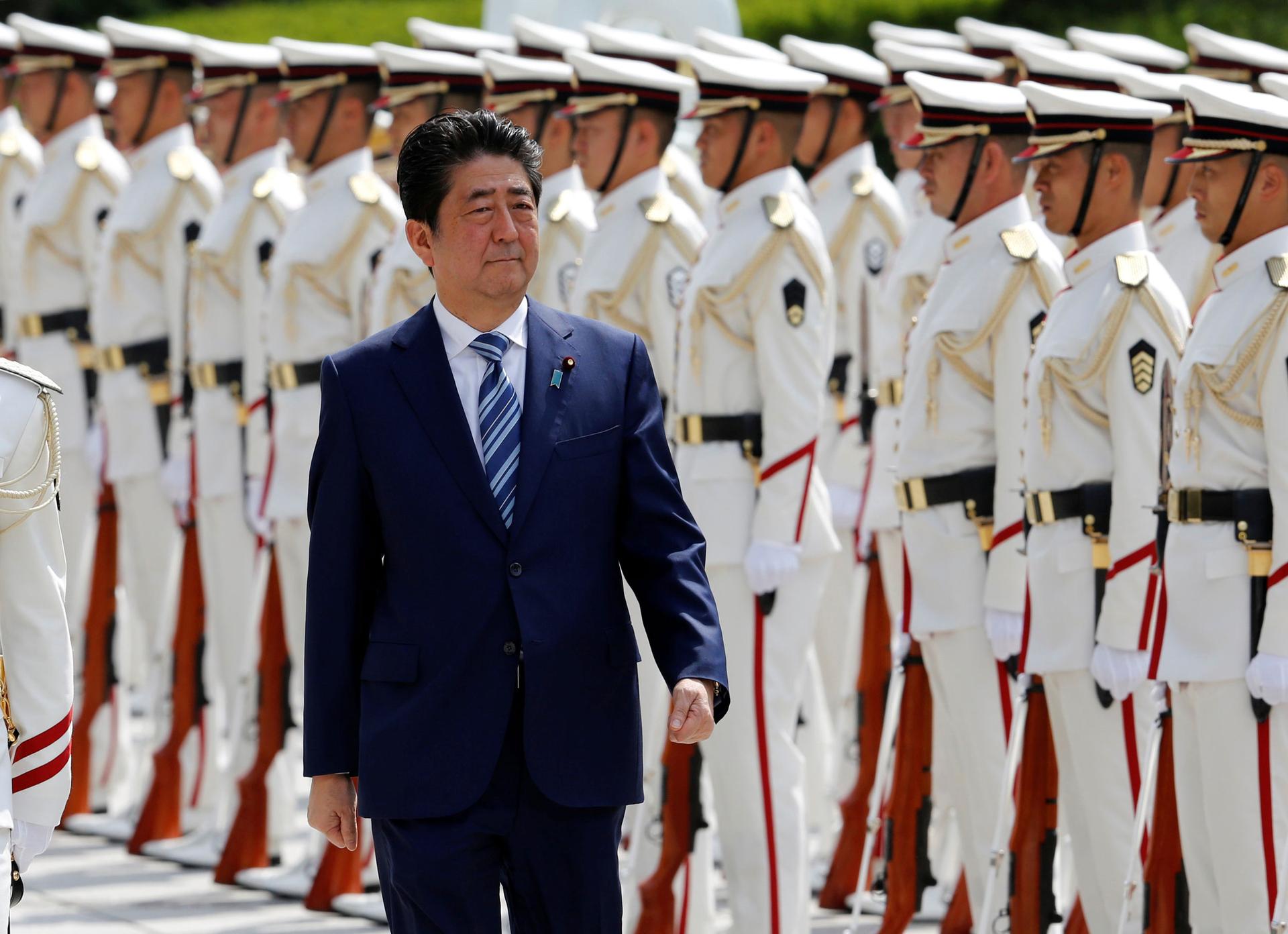 Prime Minister Shinzō Abe walks along a line of soldiers in white dress uniforms.