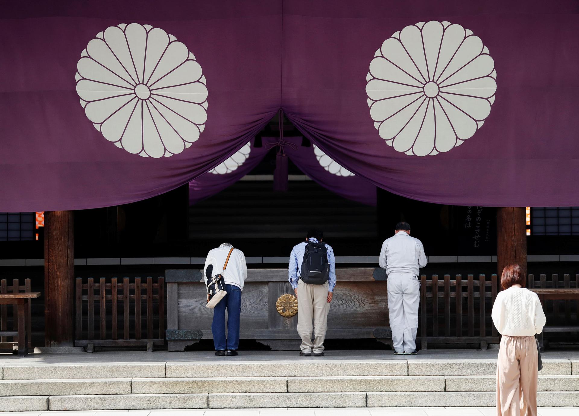 Visitors stand in of a wooden alter underneath deep purple curtains