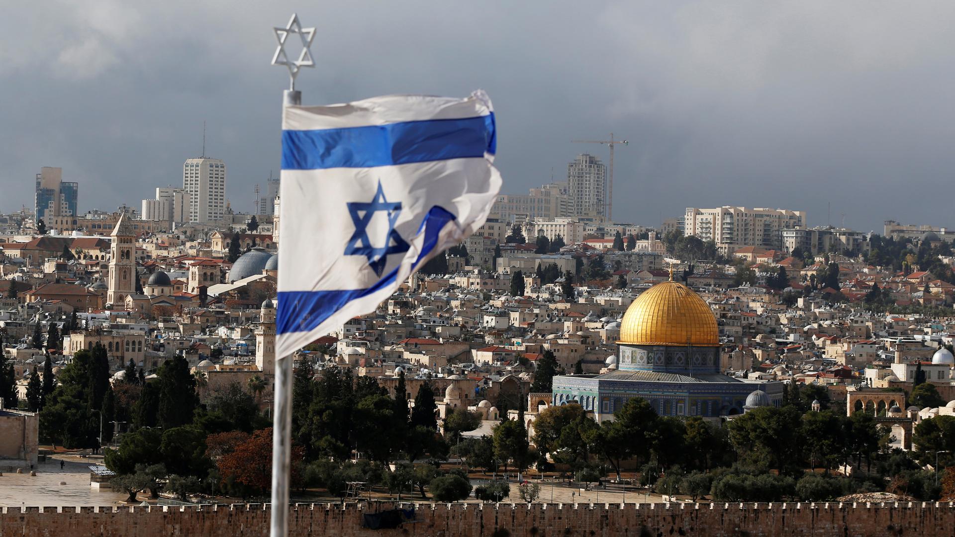 An Israeli flag is seen in the forground with the golden Dome of the Rock seen in the background.