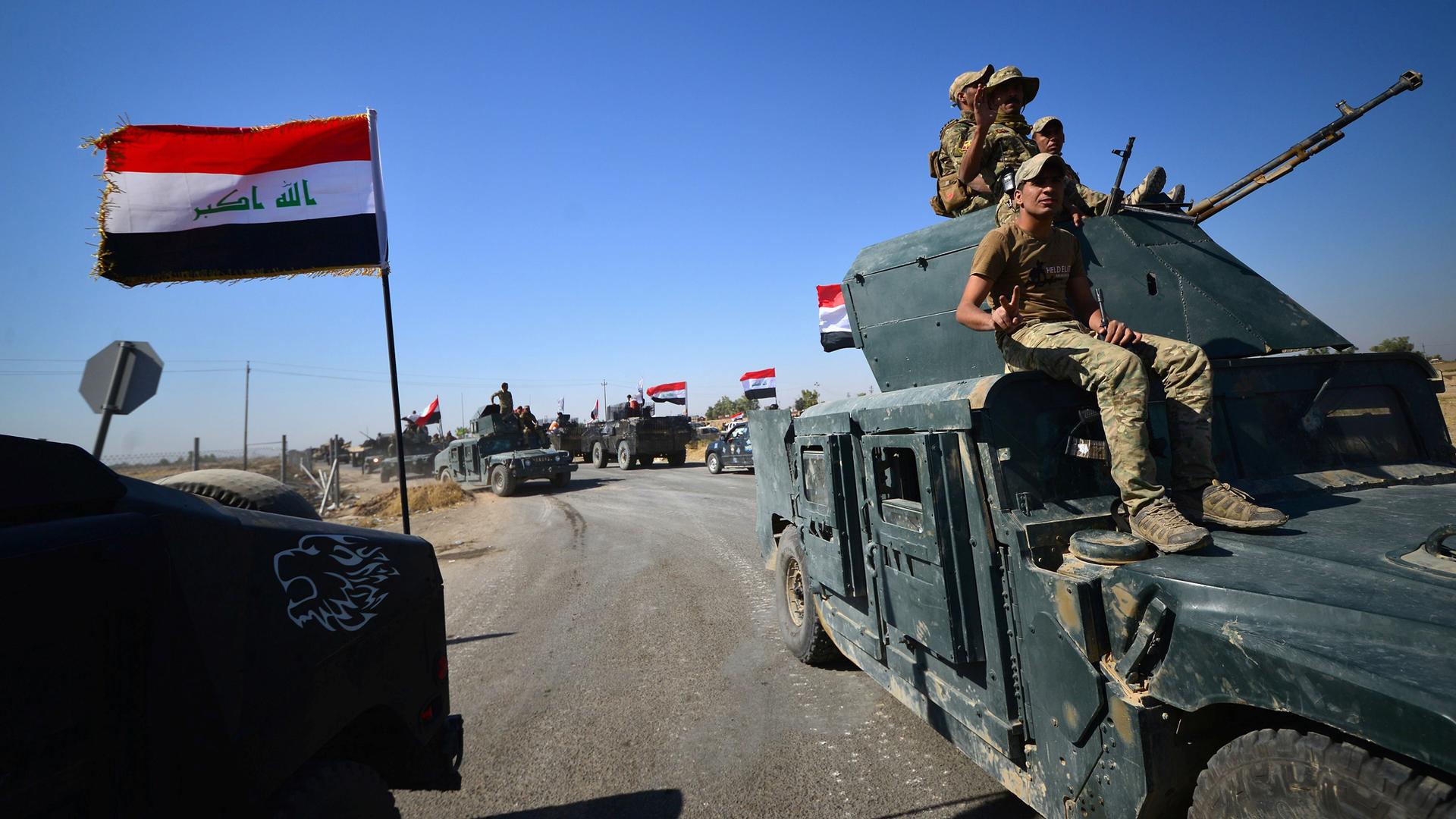 Members of Iraqi federal forces drive along desert roads in Kirkuk with Iraqi flags flying.