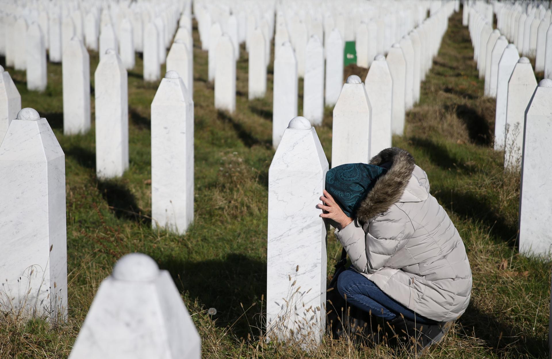 A women kneels with her head down next to a grave marker near Srebrenica.