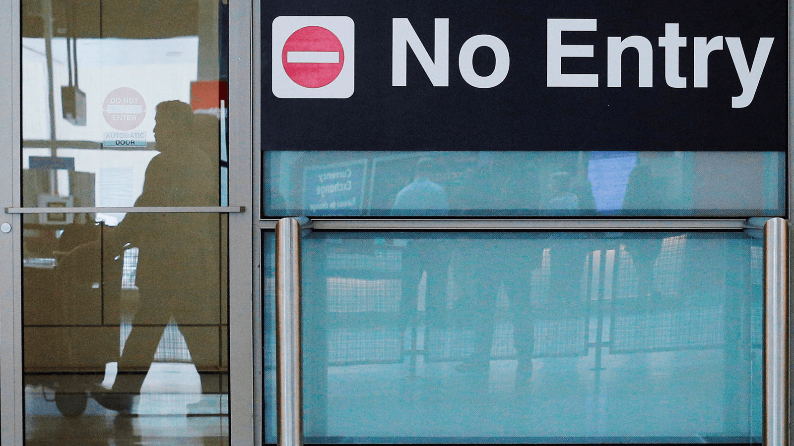 International travelers (reflected in a closed door) arrive on the day that US President Donald Trump's limited travel ban, approved by the US Supreme Court, goes into effect, at Logan Airport in Boston, Massachusetts, June 29, 2017