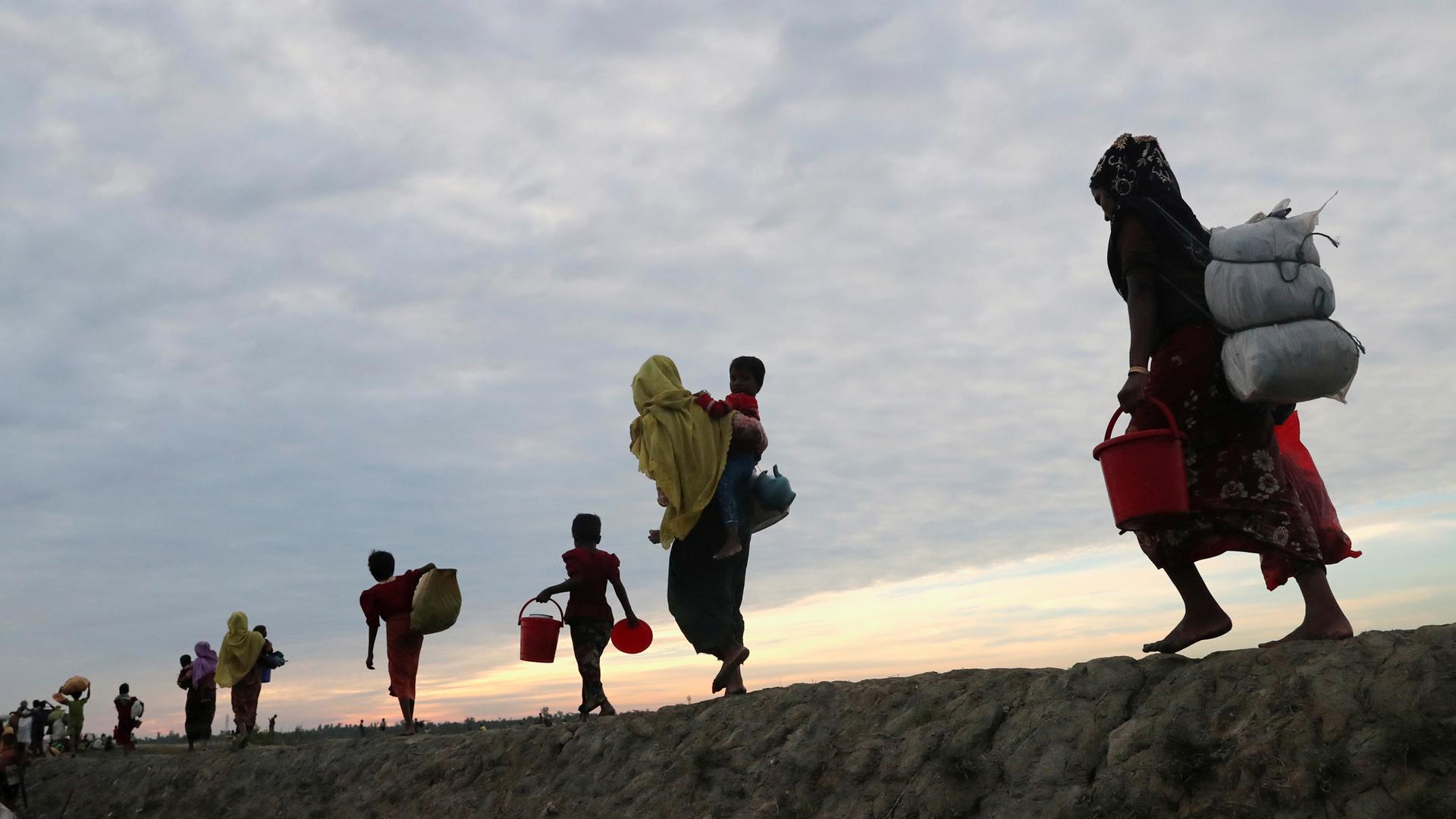 Rohingya refugees walk away from the photographer with their belongings in sacks on their backs.