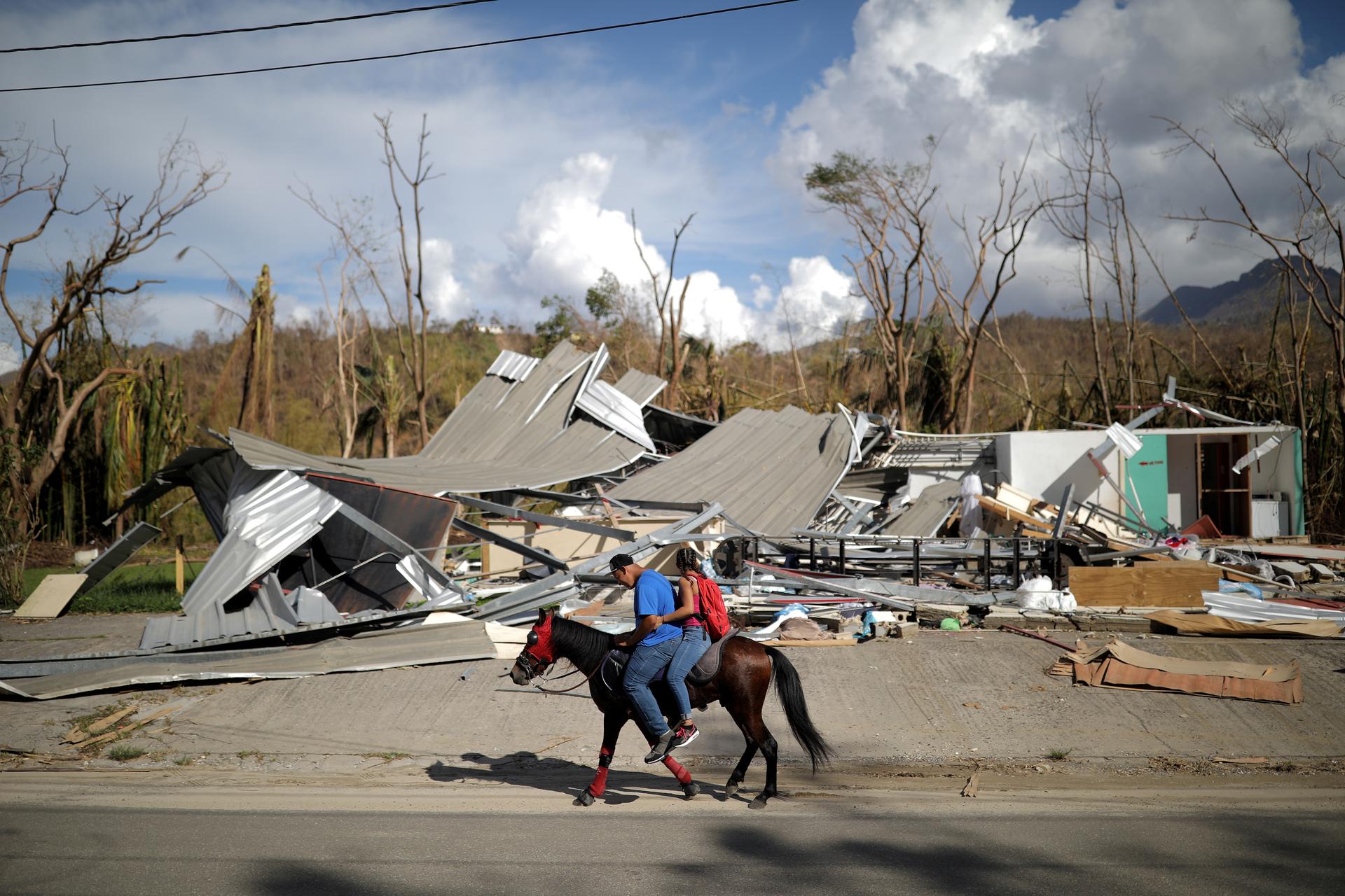 Local residents ride a horse by a destroyed building after Hurricane Maria in Jayuya, Puerto Rico