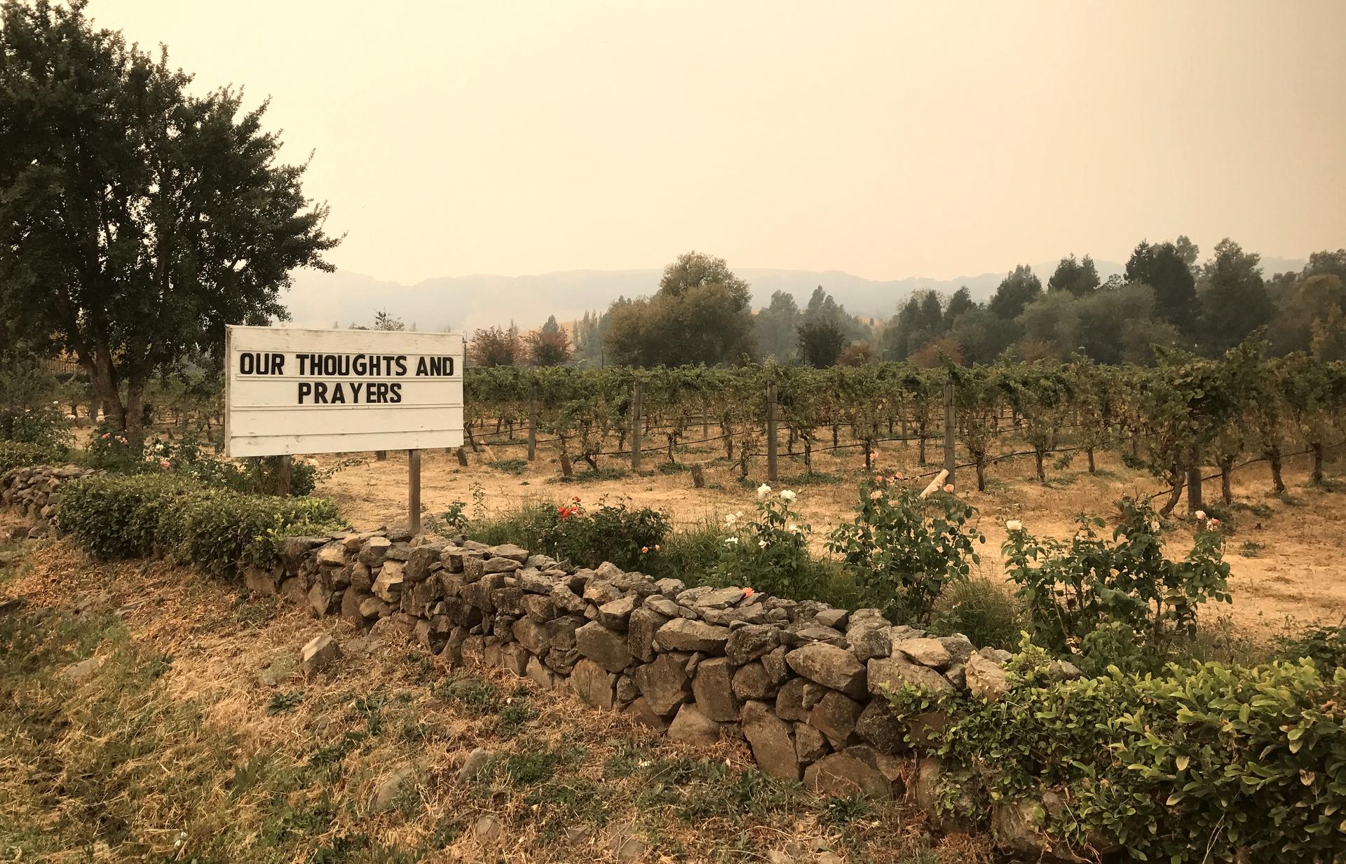 A sign outside the Cline Cellars vineyards as smoke from various wildfires fills in the distance