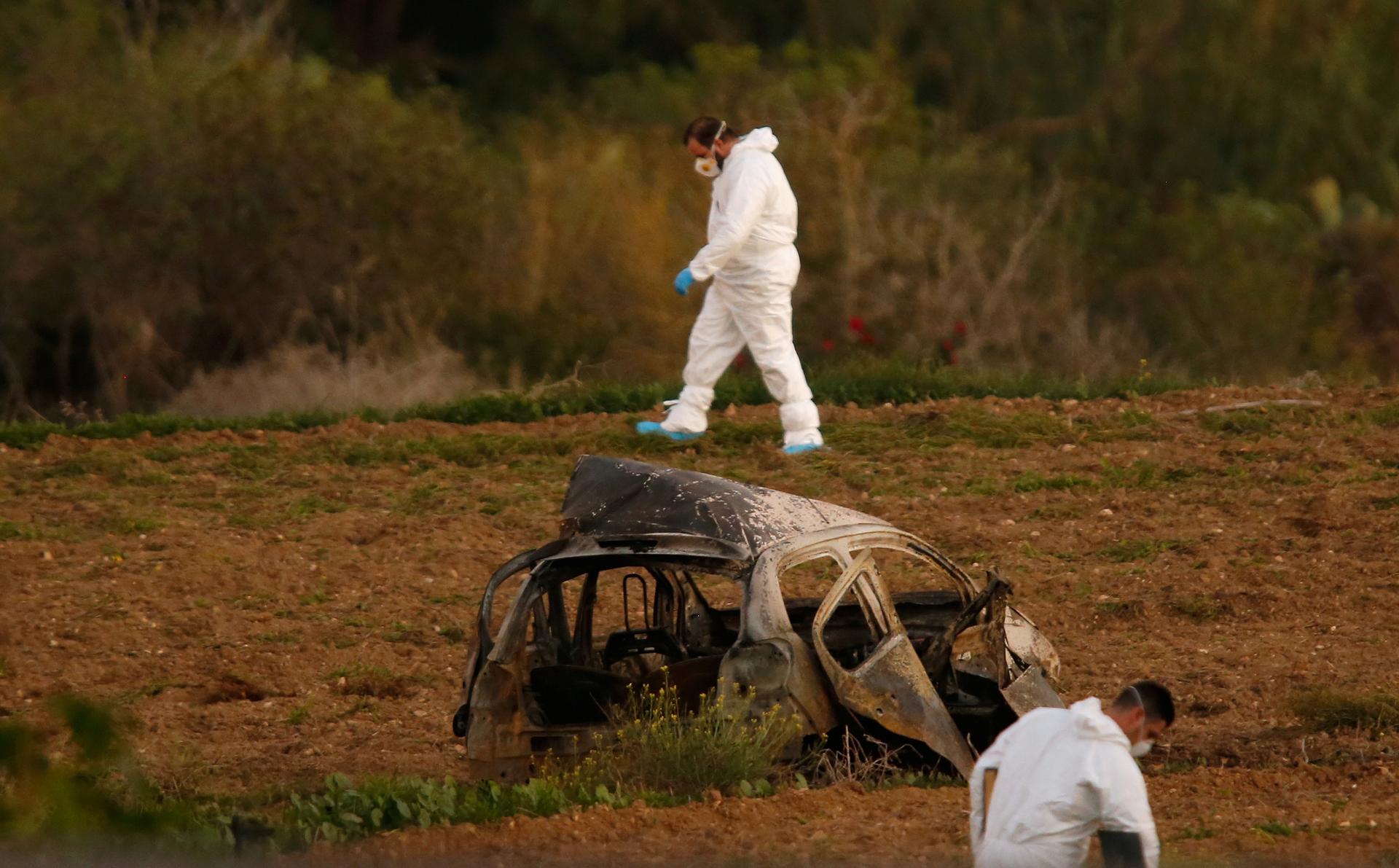 Forensic experts walk in a field after a powerful bomb blew up a car and killed investigative journalist Daphne Caruana Galizia