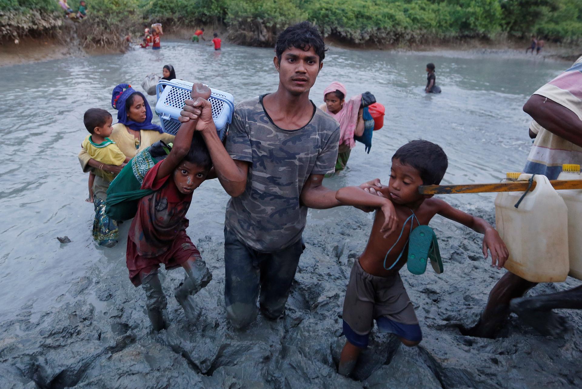 A Rohingya refugee helps children cross the mud after crossing the Naf River at the Bangladesh-Myanmar border. 
