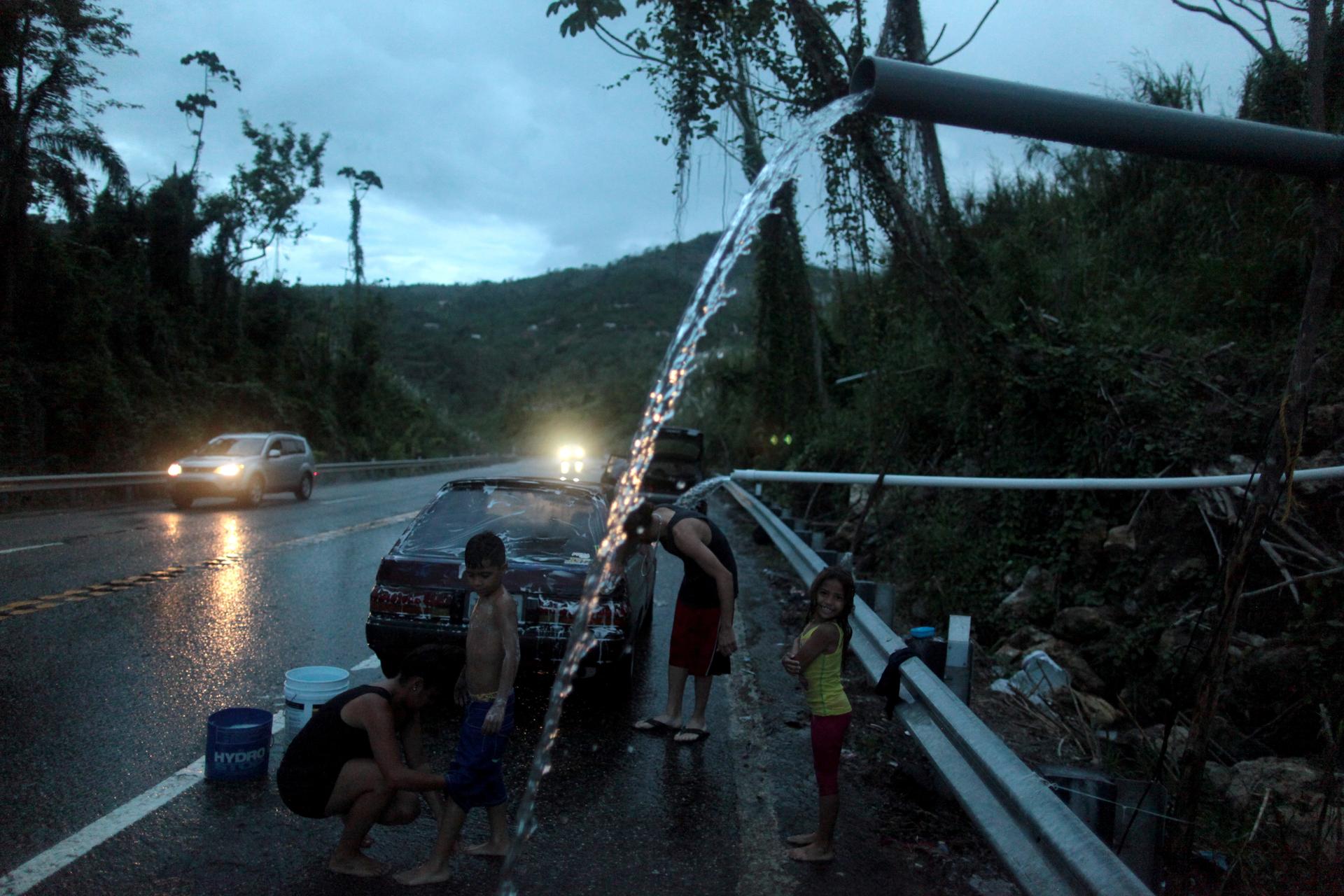 A family bathe and wash their car with mountain spring water after hurricane Maria hit the area in September, in Utuado, Puerto Rico.