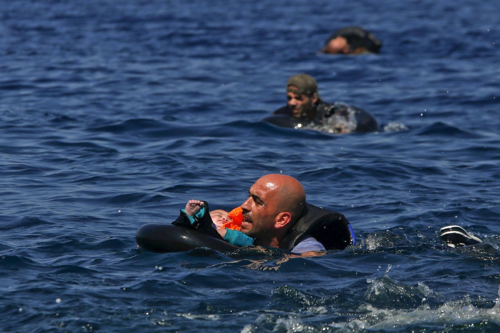 A Syrian refugee holding a baby in a life tube swims towards the shore, after their dinghy deflated some 100 yards from the Greek island of Lesbos, September 13th 2015. 