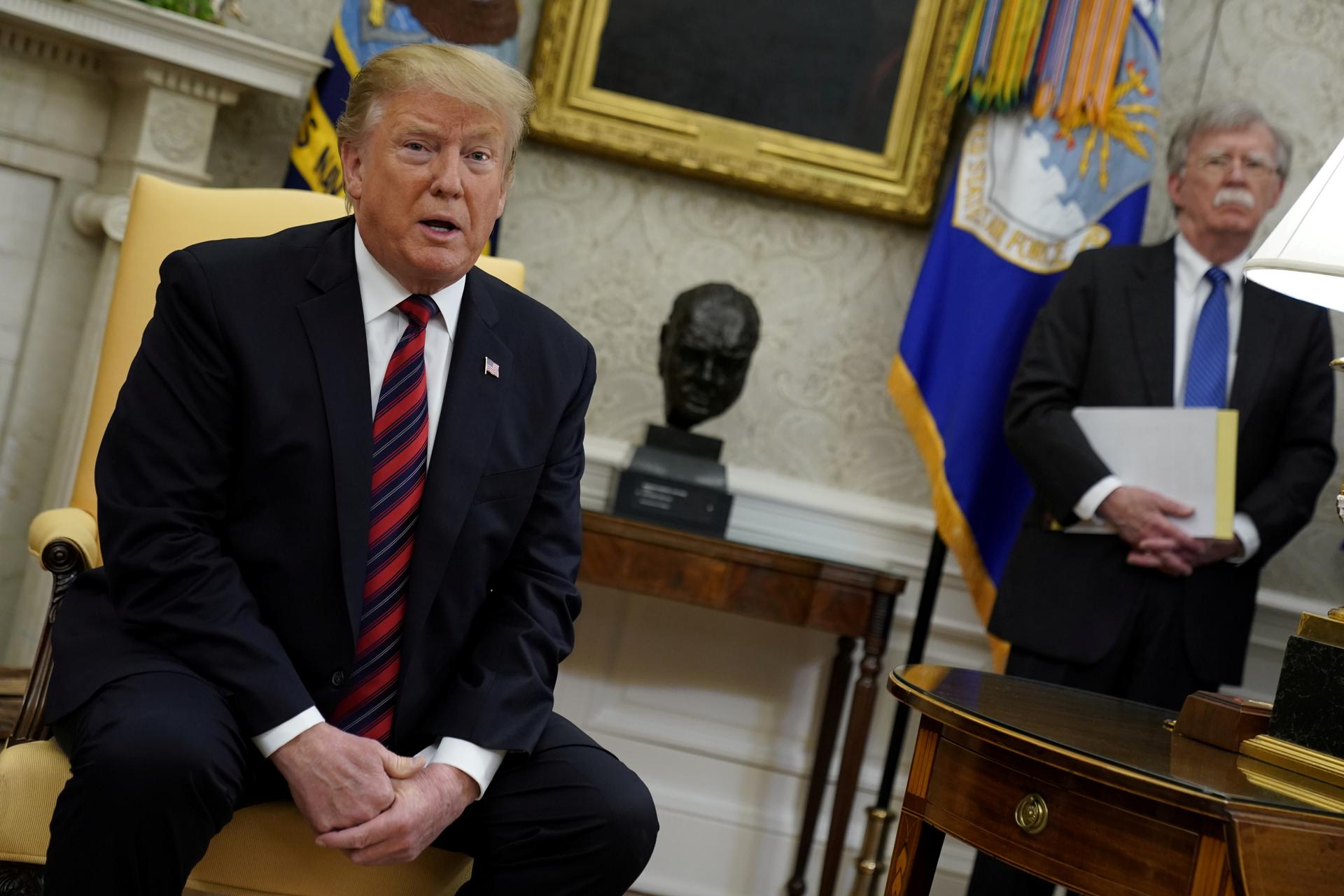 US President Donald Trump speaks to reporters with National Security Adviser John Bolton looking on in the Oval Office at the White House