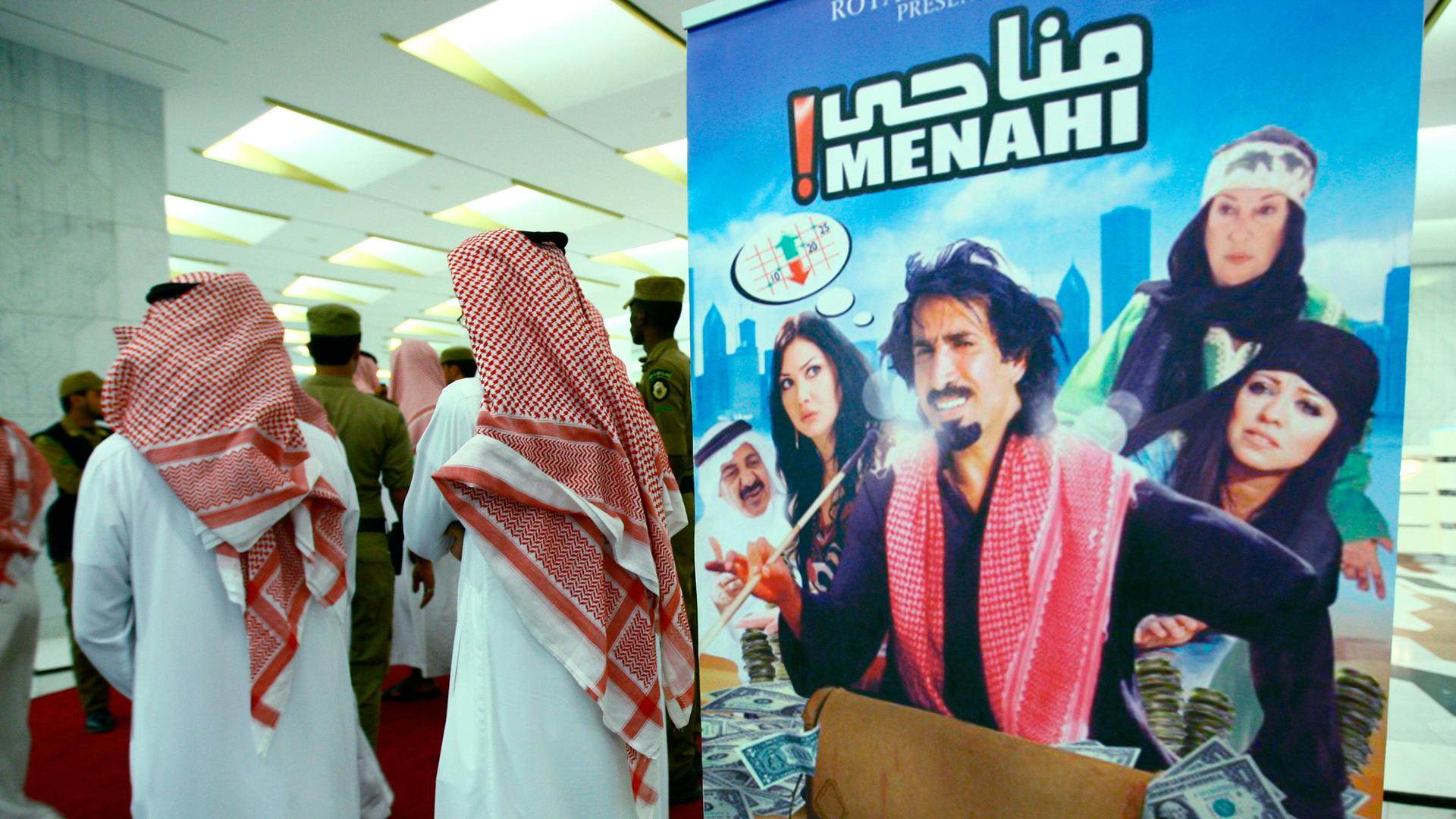 Saudi religious men stand near a poster of the first Saudi film "Menhai" at its opening at King Fahad Center in Riyadh June 6, 2009.