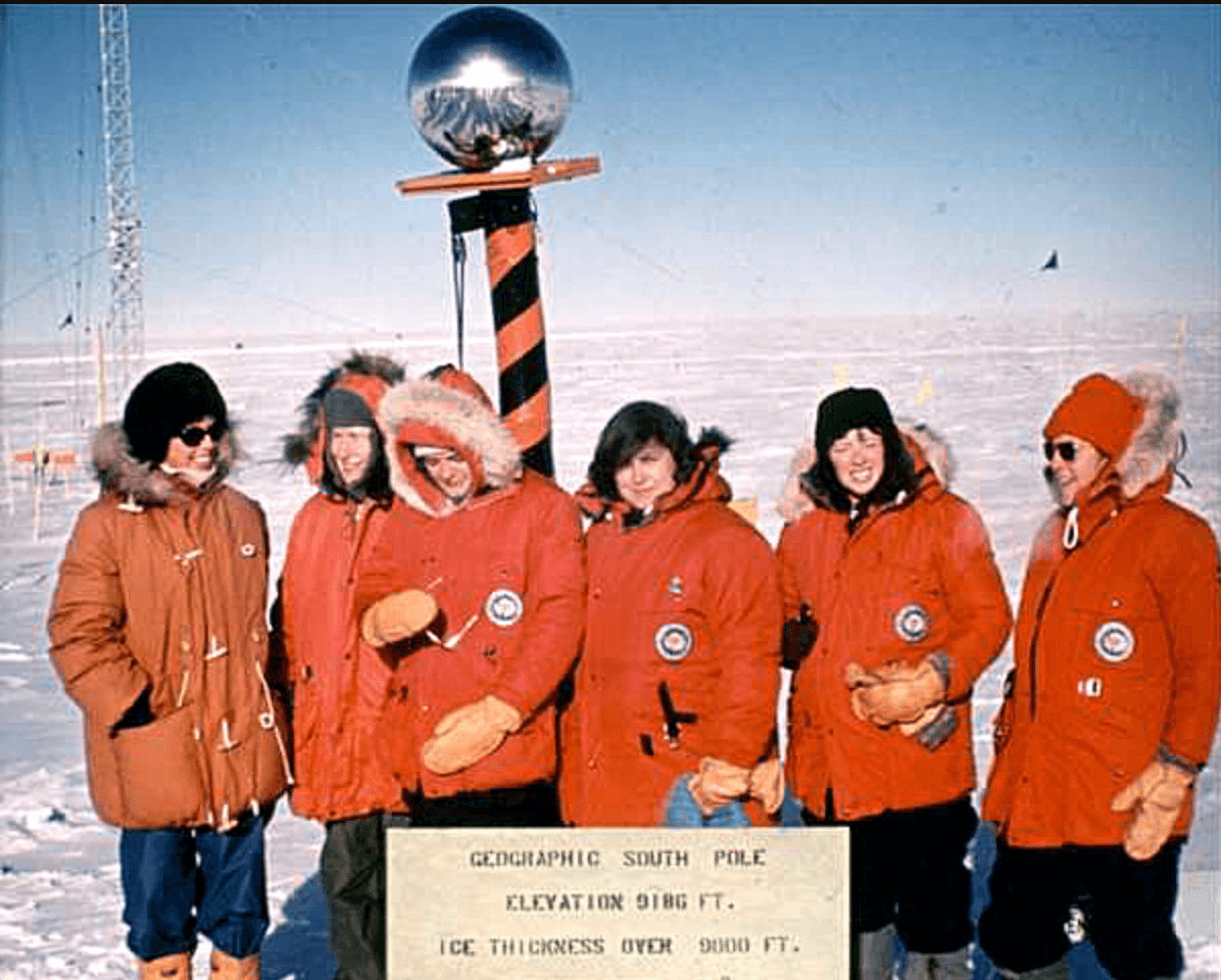 Five women with red parkas pose for a photo at the South Pole.
